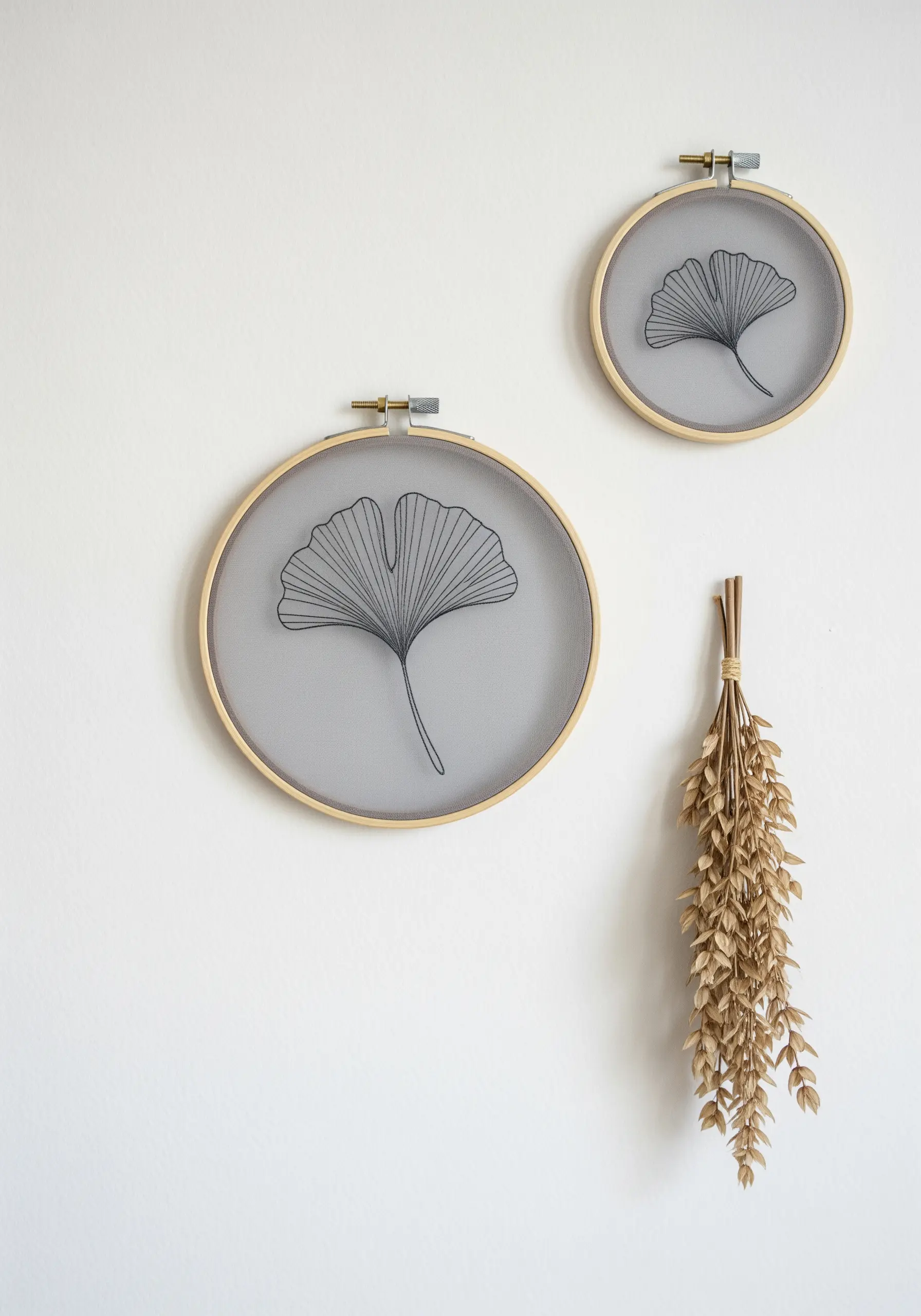 Two ginkgo leaves embroidered in black thread on sheer gray fabric and framed in wooden hoops.