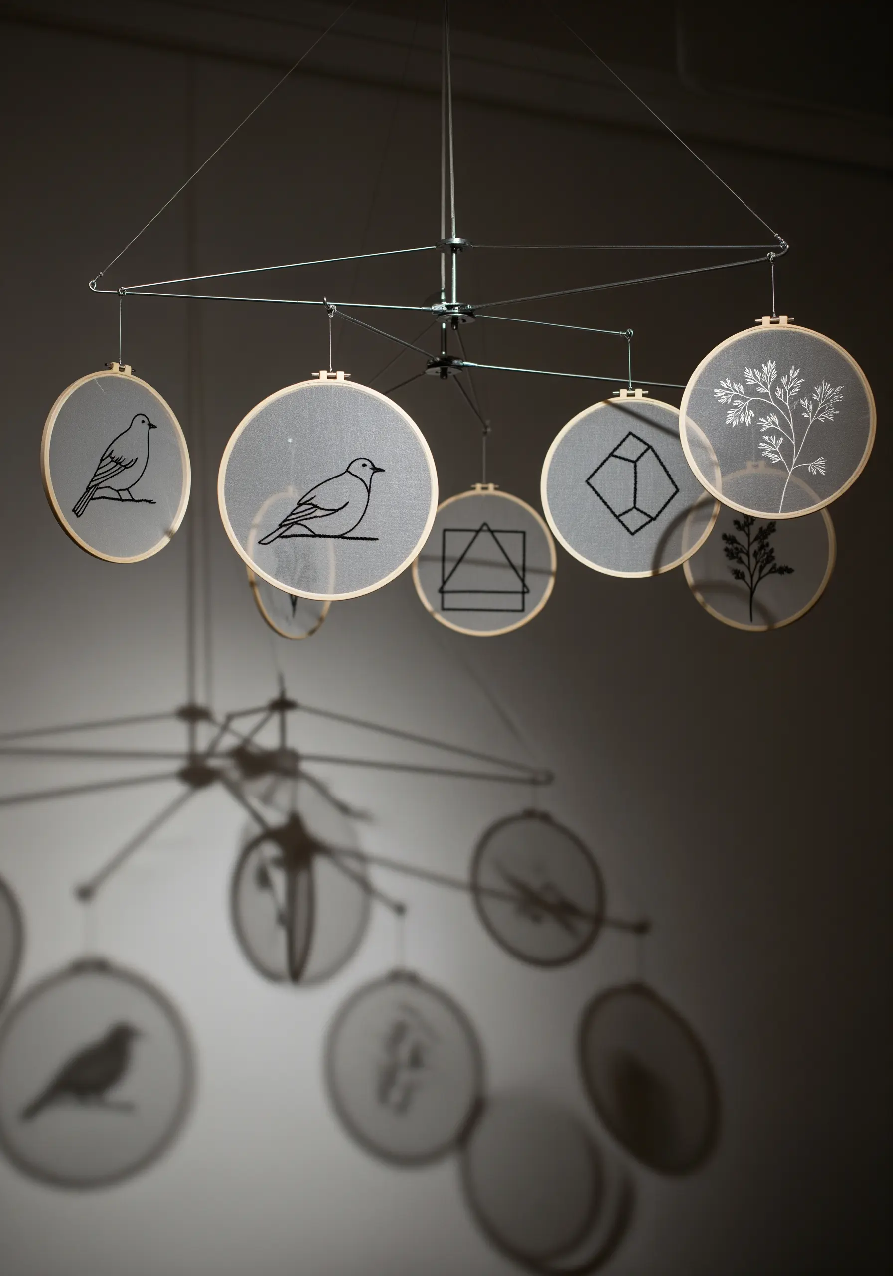 A mobile made of embroidery hoops with minimalist designs stitched on sheer fabric, casting shadows.
