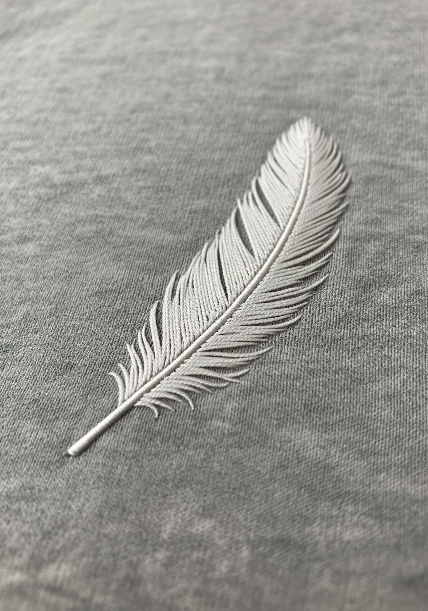 A delicate, realistic white feather embroidered on a grey knit fabric.