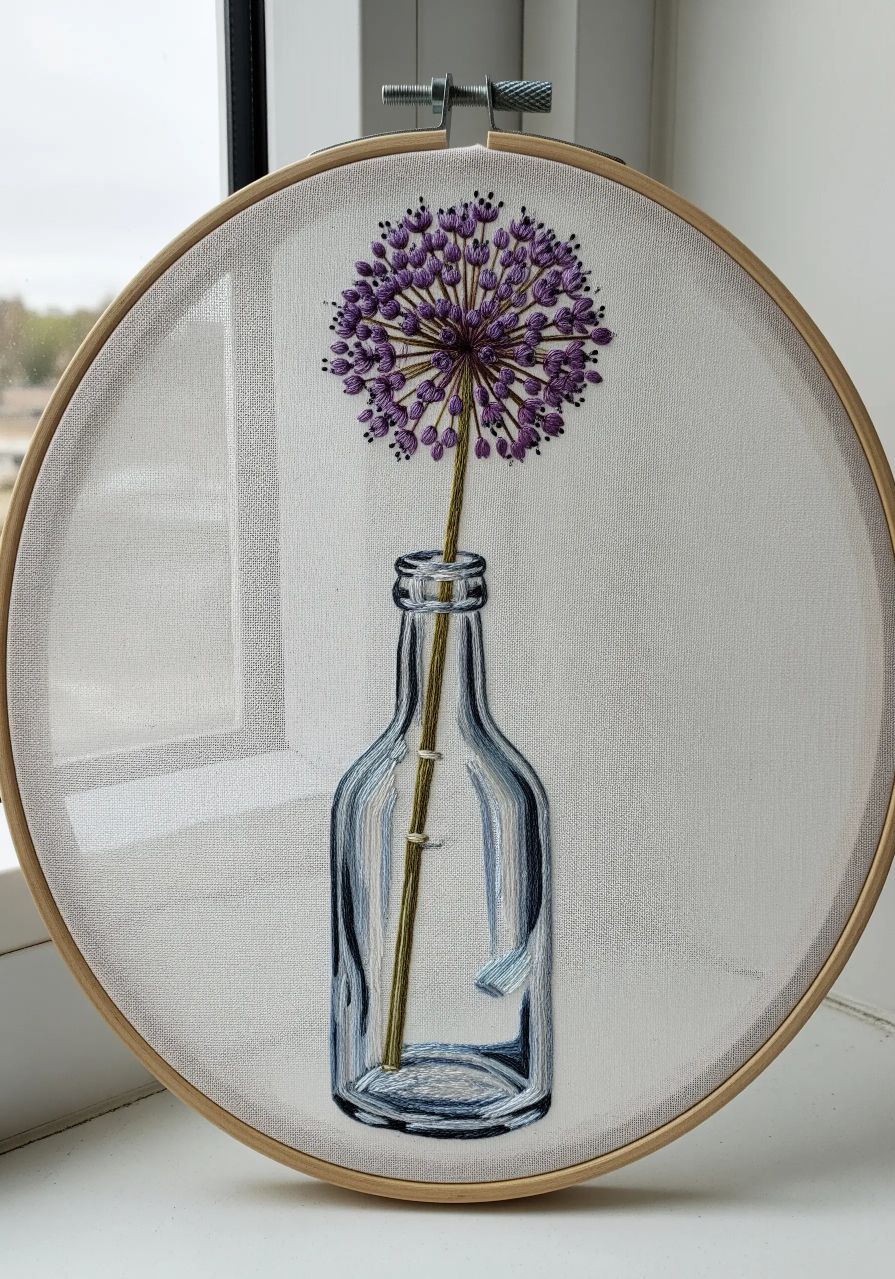 Embroidery of a purple allium flower in a realistic glass bottle