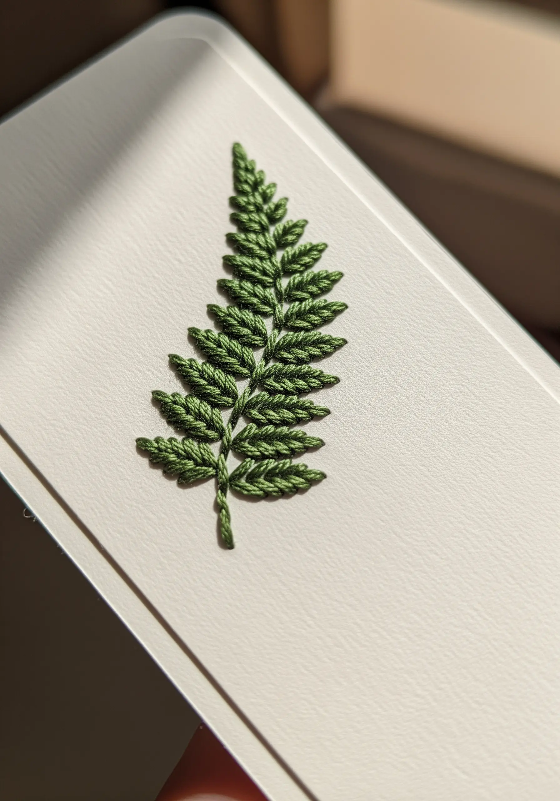A vibrant green fern, perfectly embroidered on a piece of smooth, off-white cardstock.