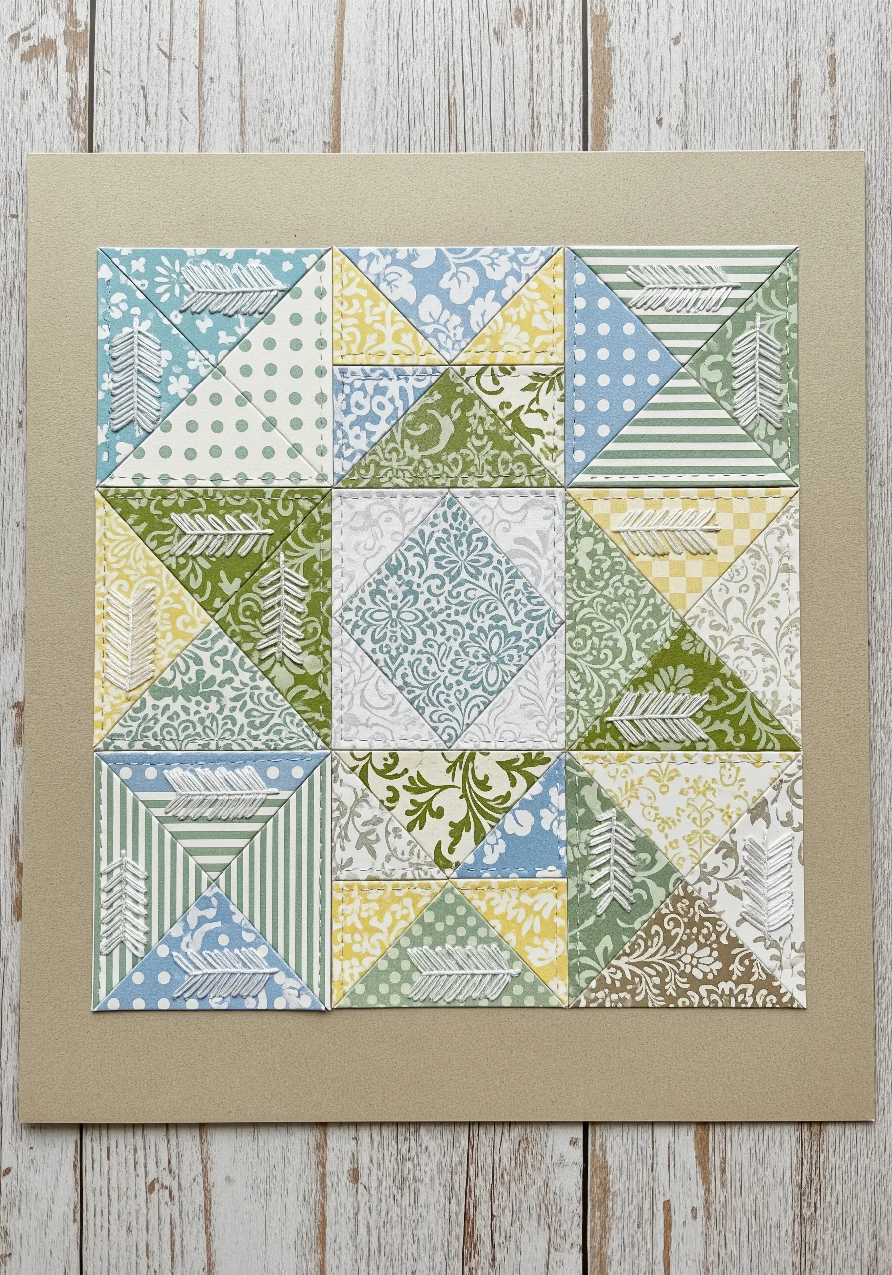 A paper quilt block made of patterned squares with delicate white stitched feather motifs.