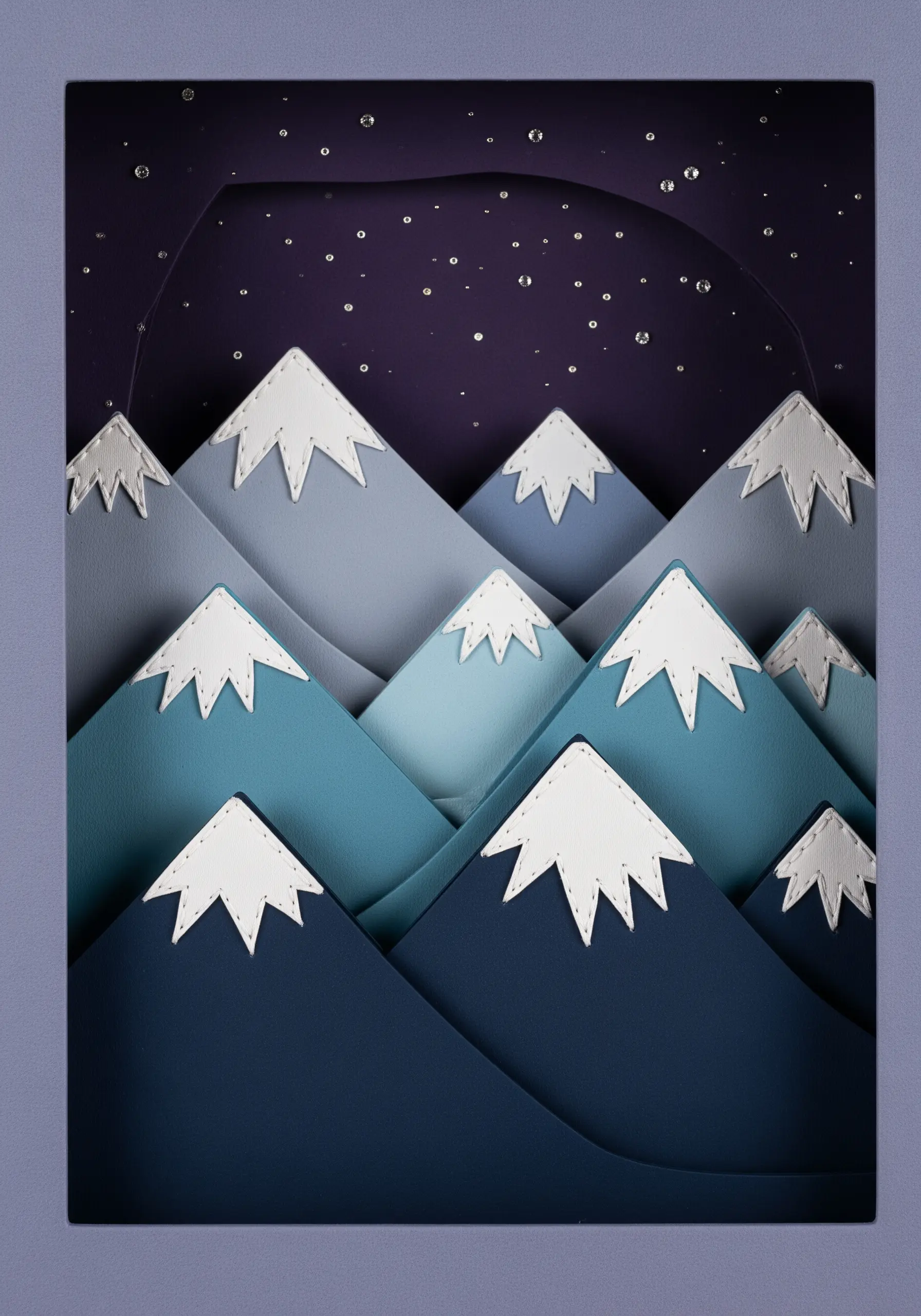 A layered paper art scene of mountains, with the white snow caps attached using visible stitches.