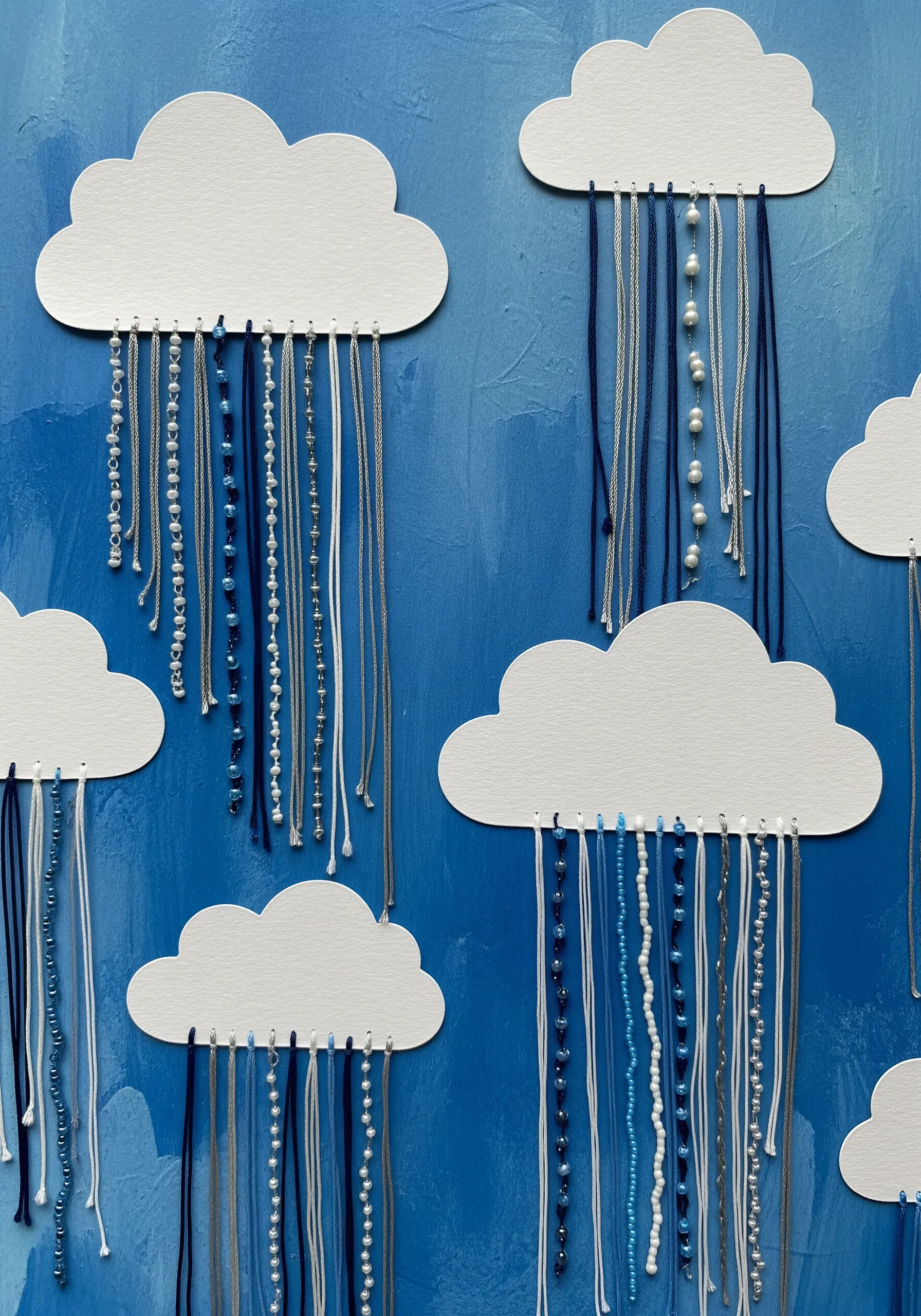 White paper clouds with threads and beads hanging down to represent rain.