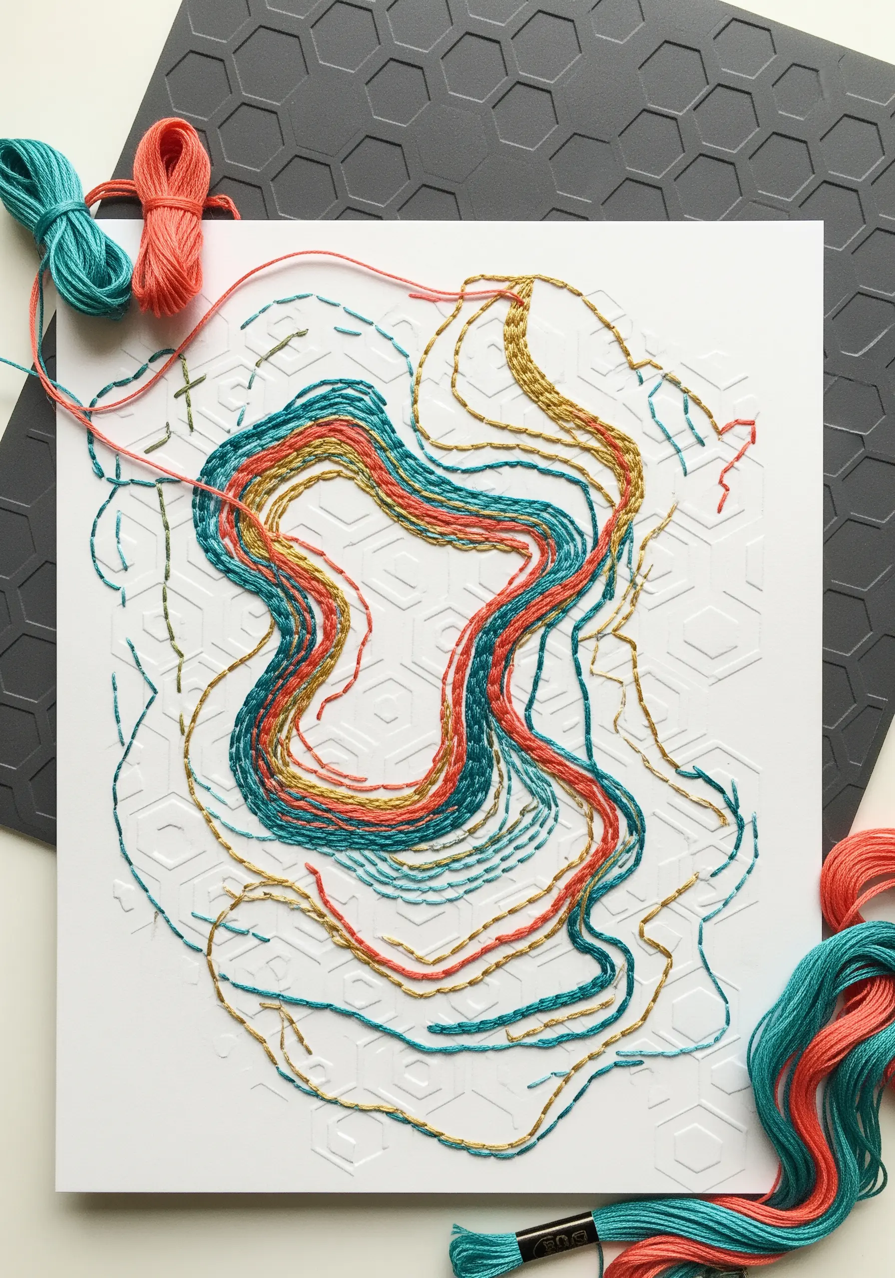 Abstract thread art in coral, teal, and gold stitched over white geometric embossed paper.