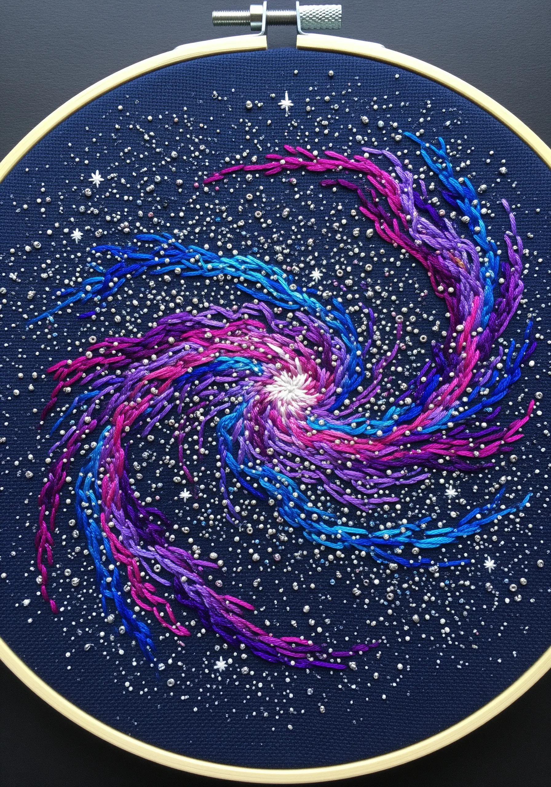 Embroidered spiral galaxy in vibrant colors with French knot stars on dark fabric.