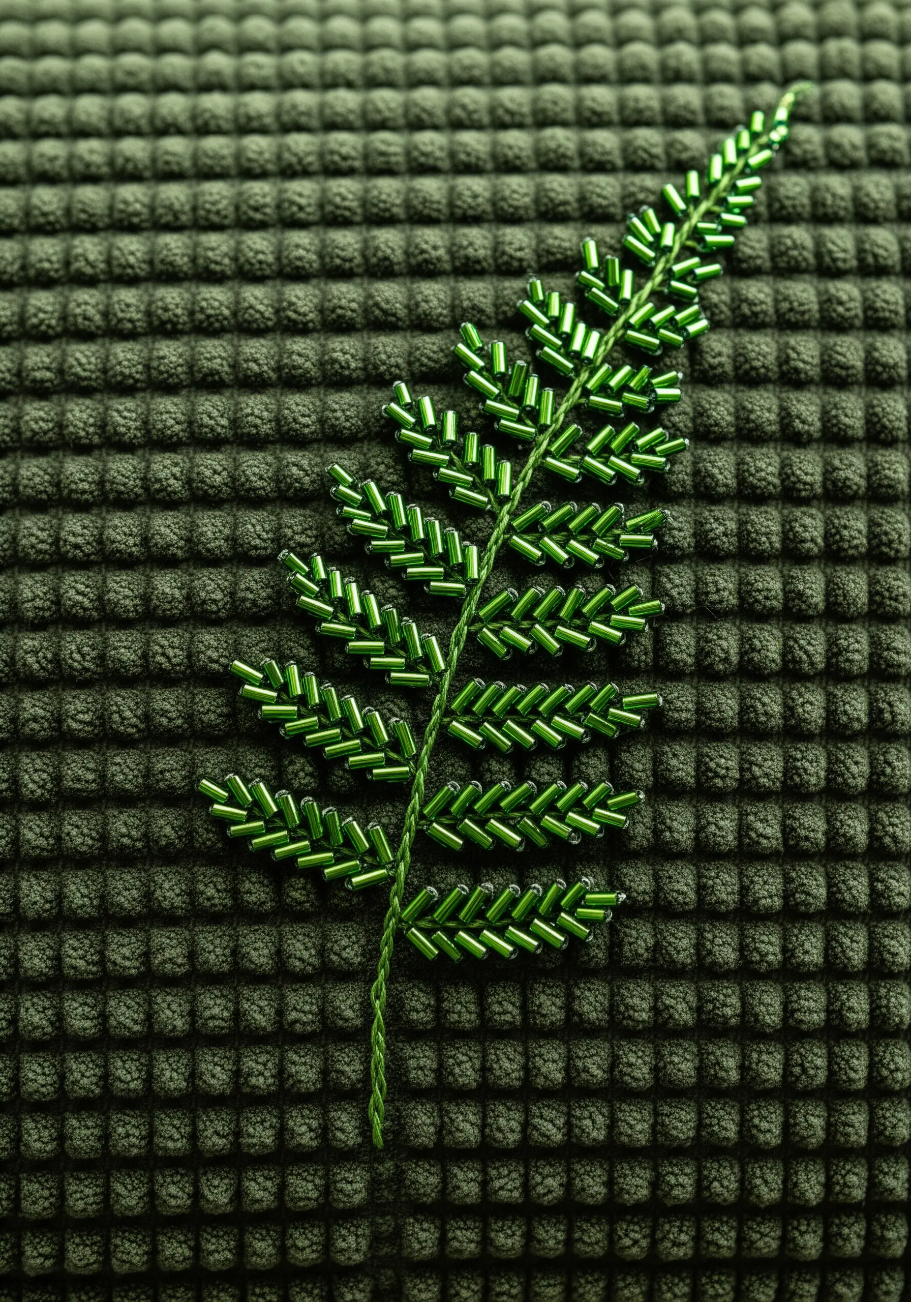 A fern leaf motif created entirely with green bugle beads on a textured green fabric.