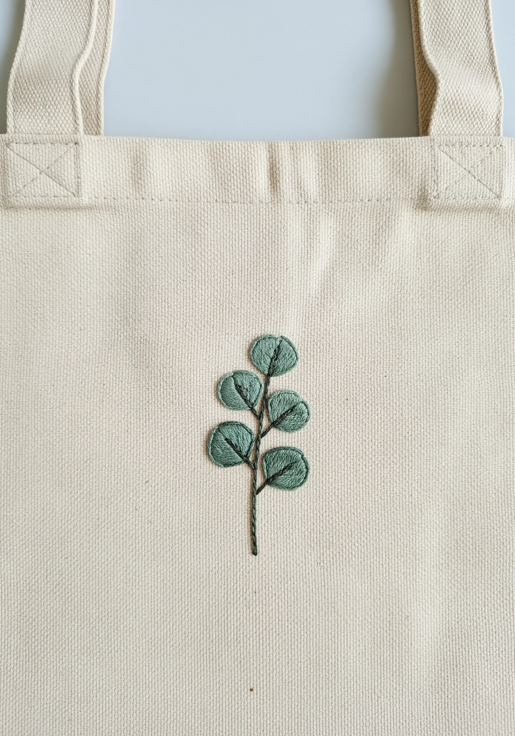 A single branch of eucalyptus with subtly shaded green leaves on a canvas tote.