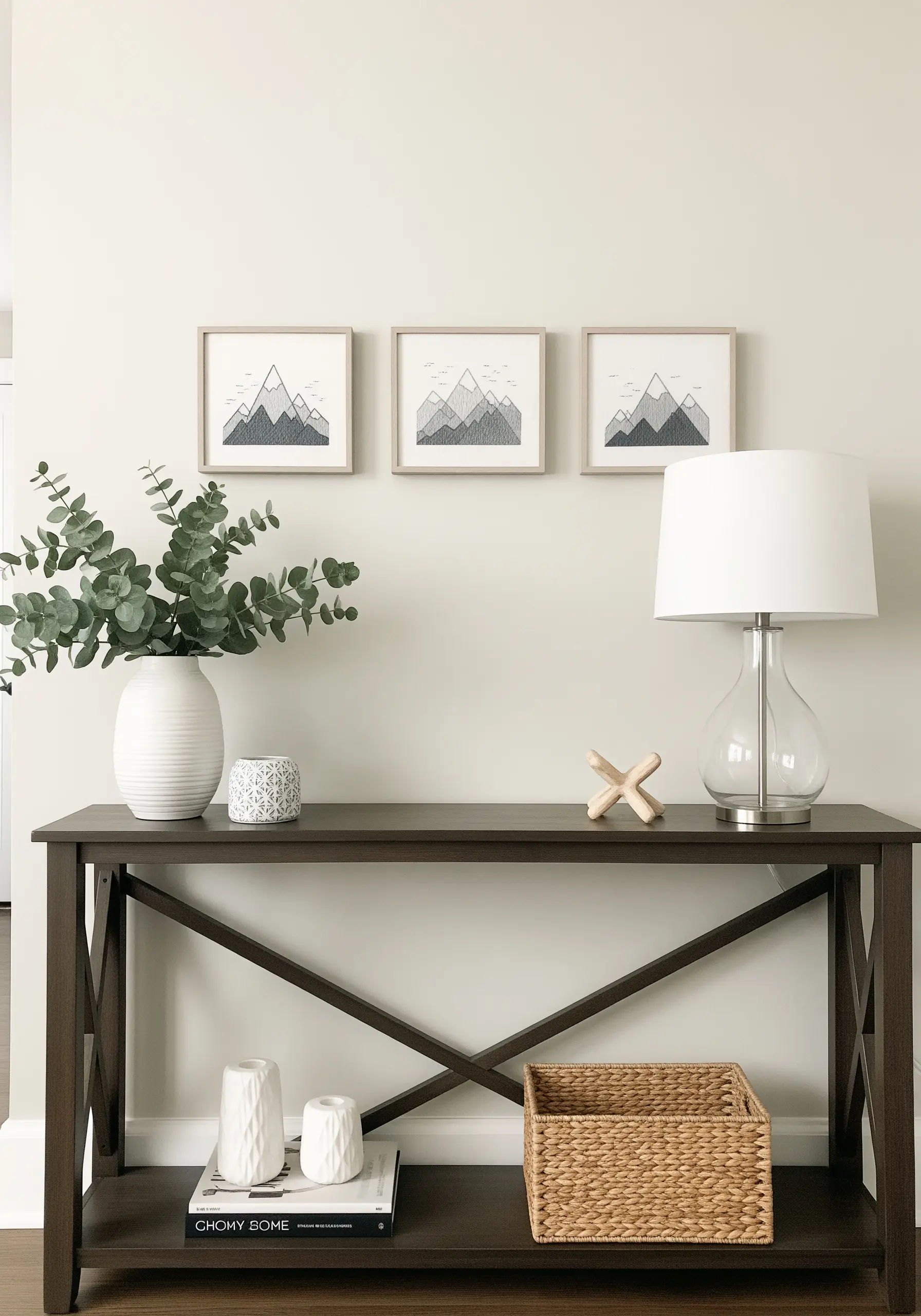 A set of three framed embroideries with minimalist, line-art mountains on a console table