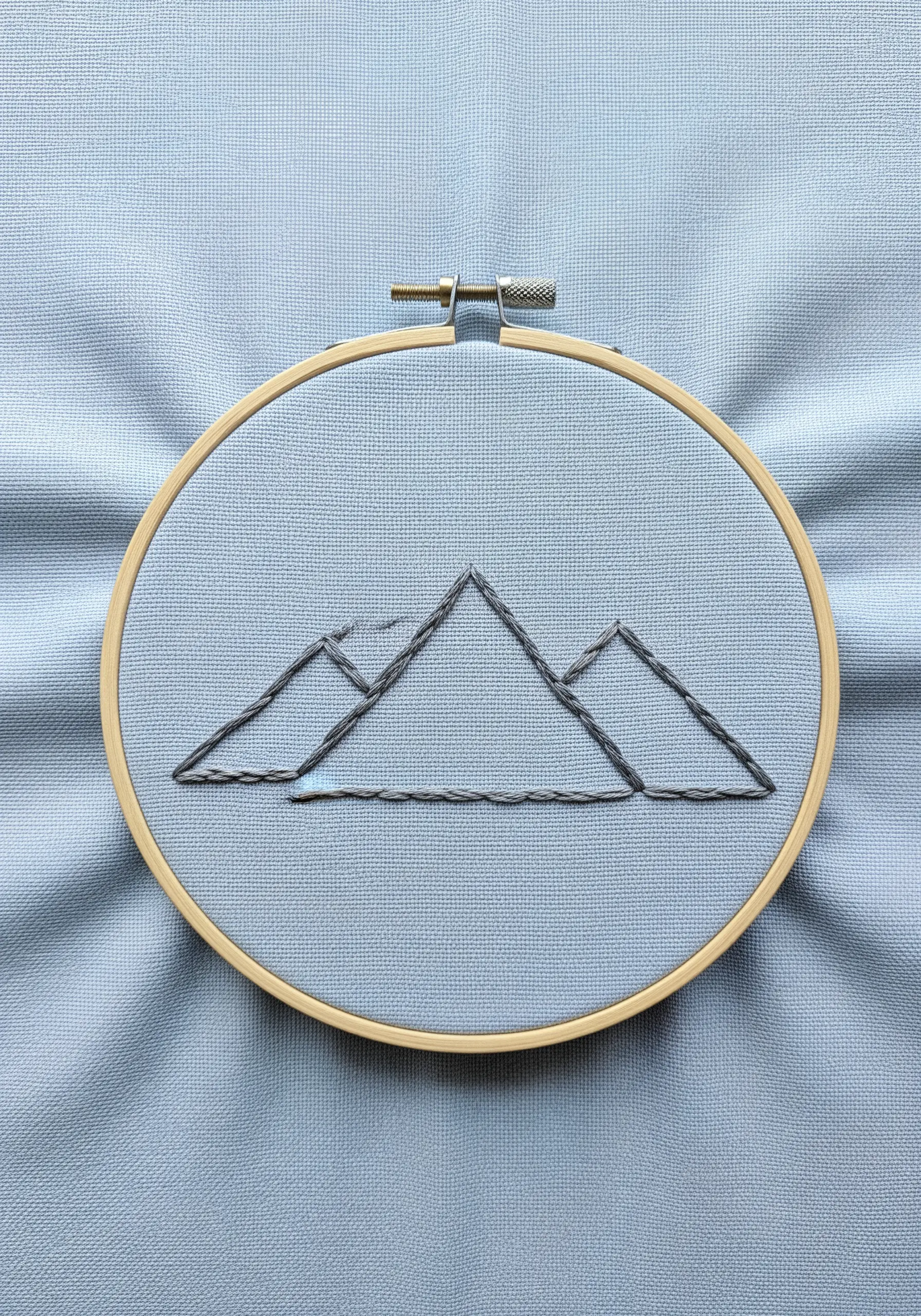 A minimalist mountain range outline stitched in grey variegated thread.