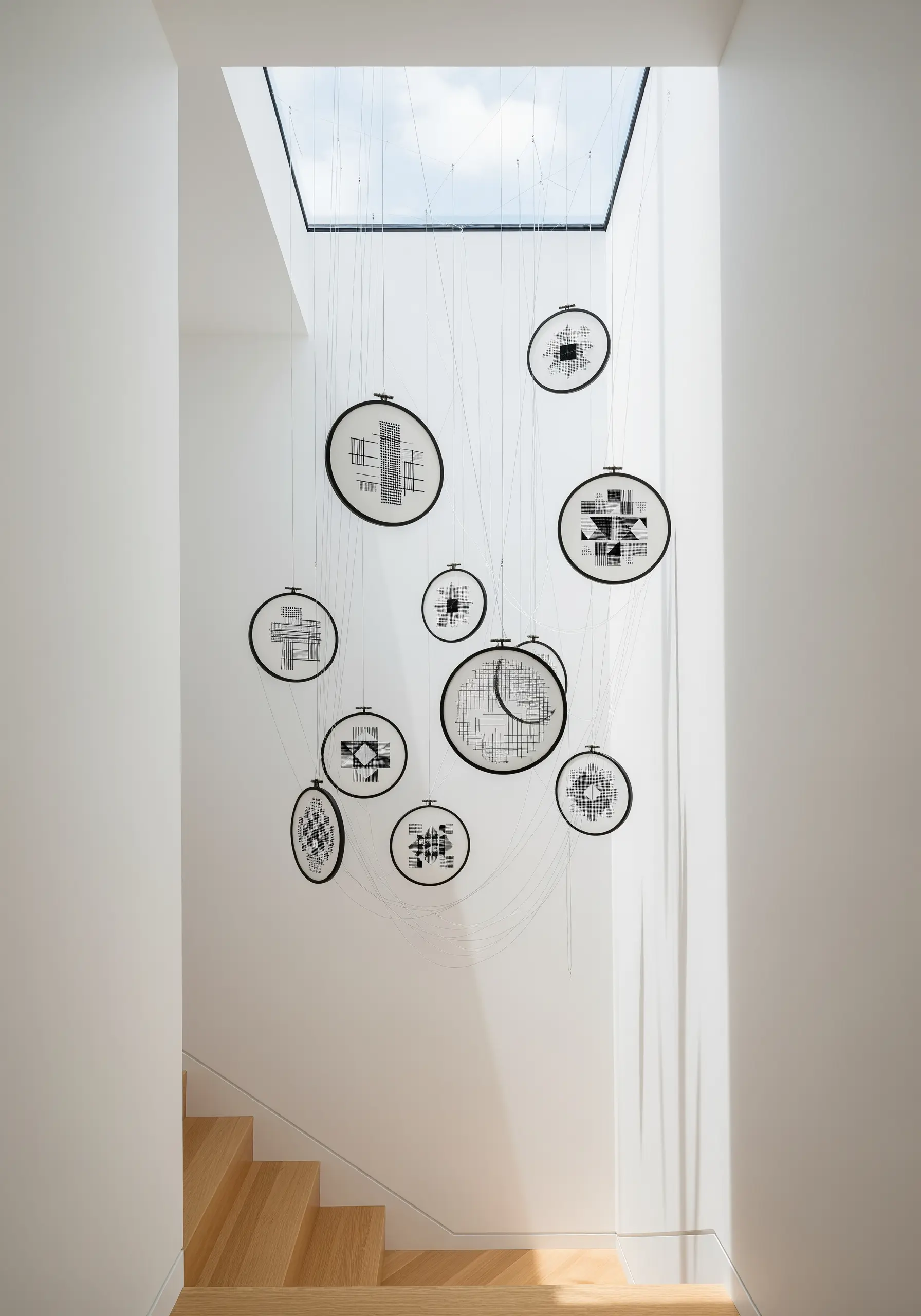 A collection of blackwork embroidery hoops suspended from the ceiling in a modern stairwell