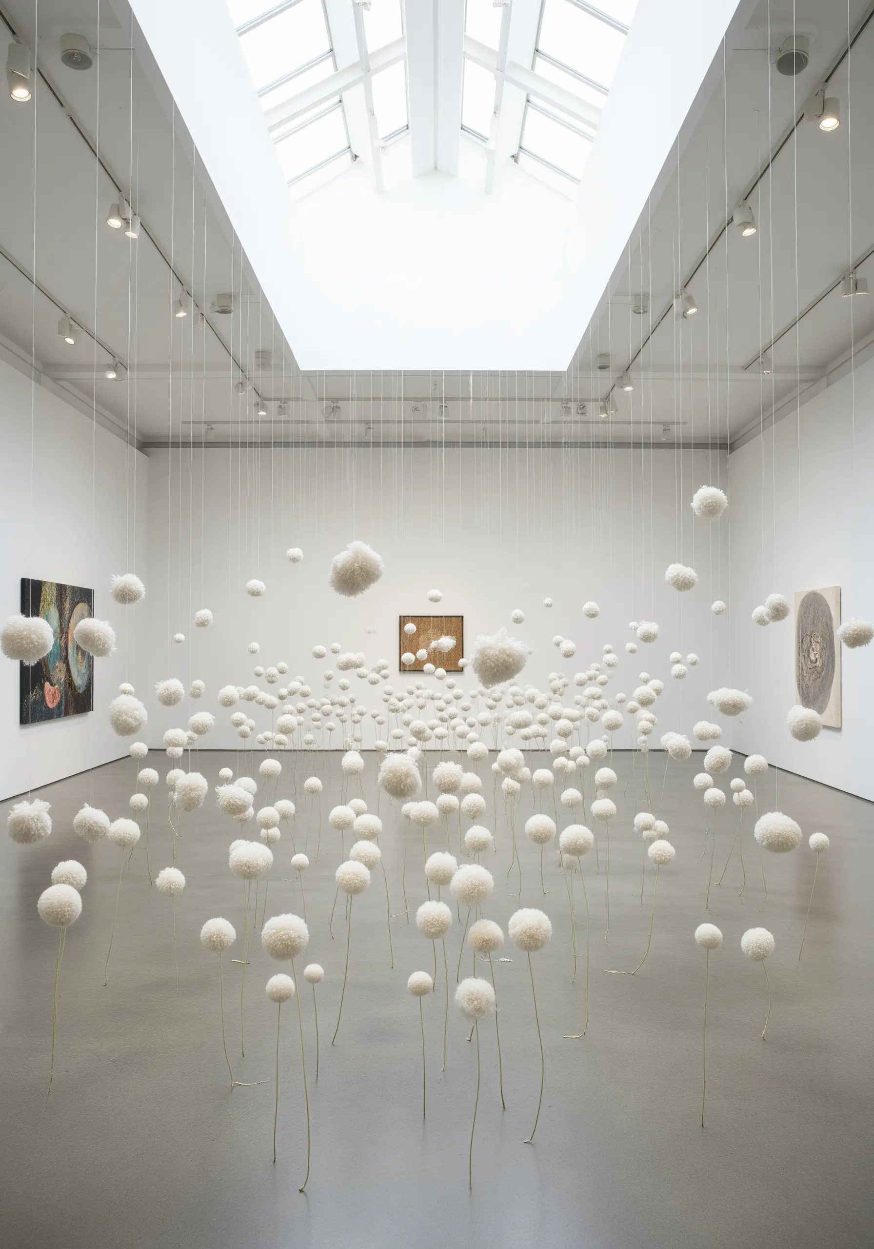 A gallery filled with hundreds of white, fluffy pom-poms suspended from the ceiling like dandelions.