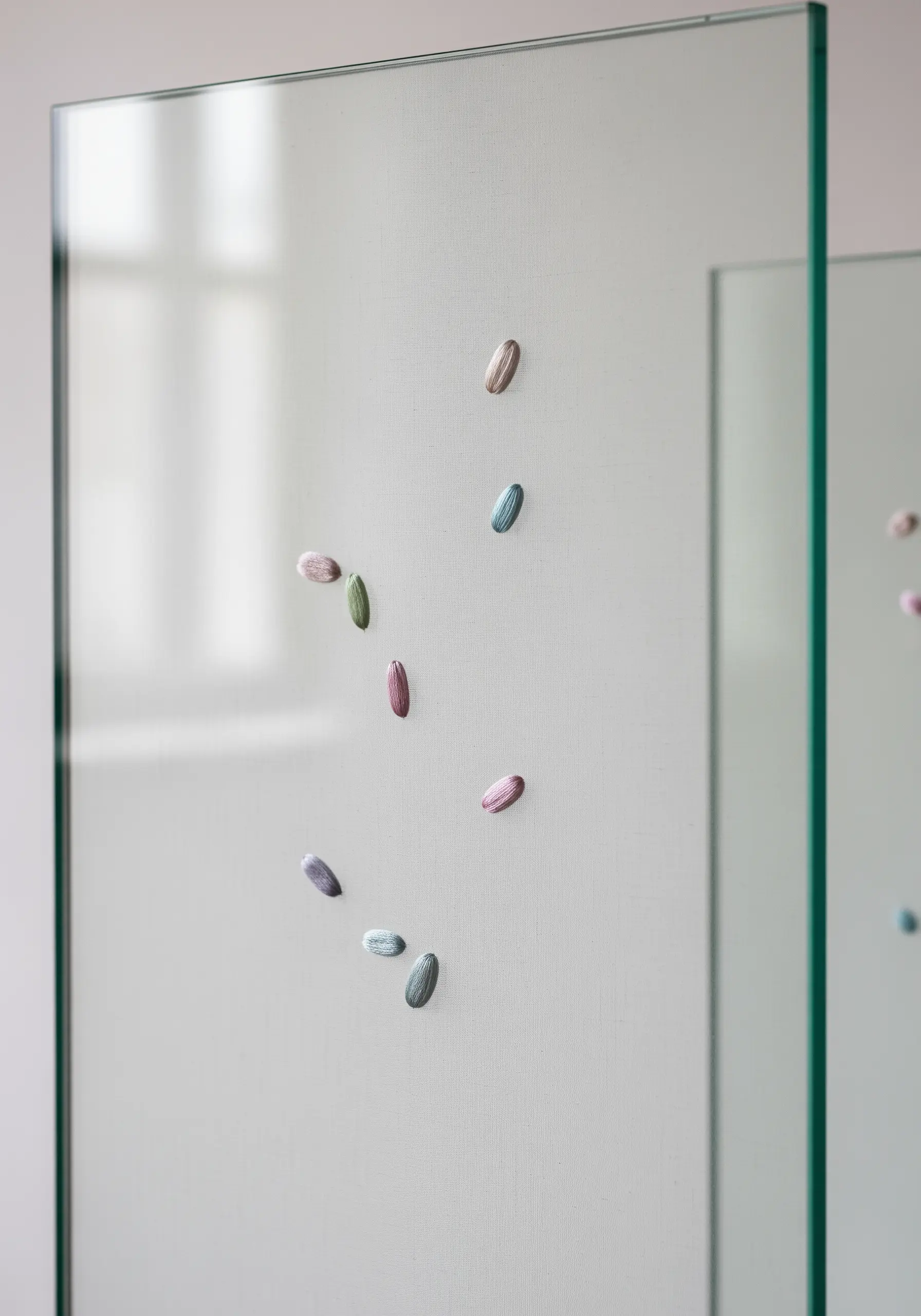 Small, colorful satin-stitched shapes appearing to float against a translucent glass panel.