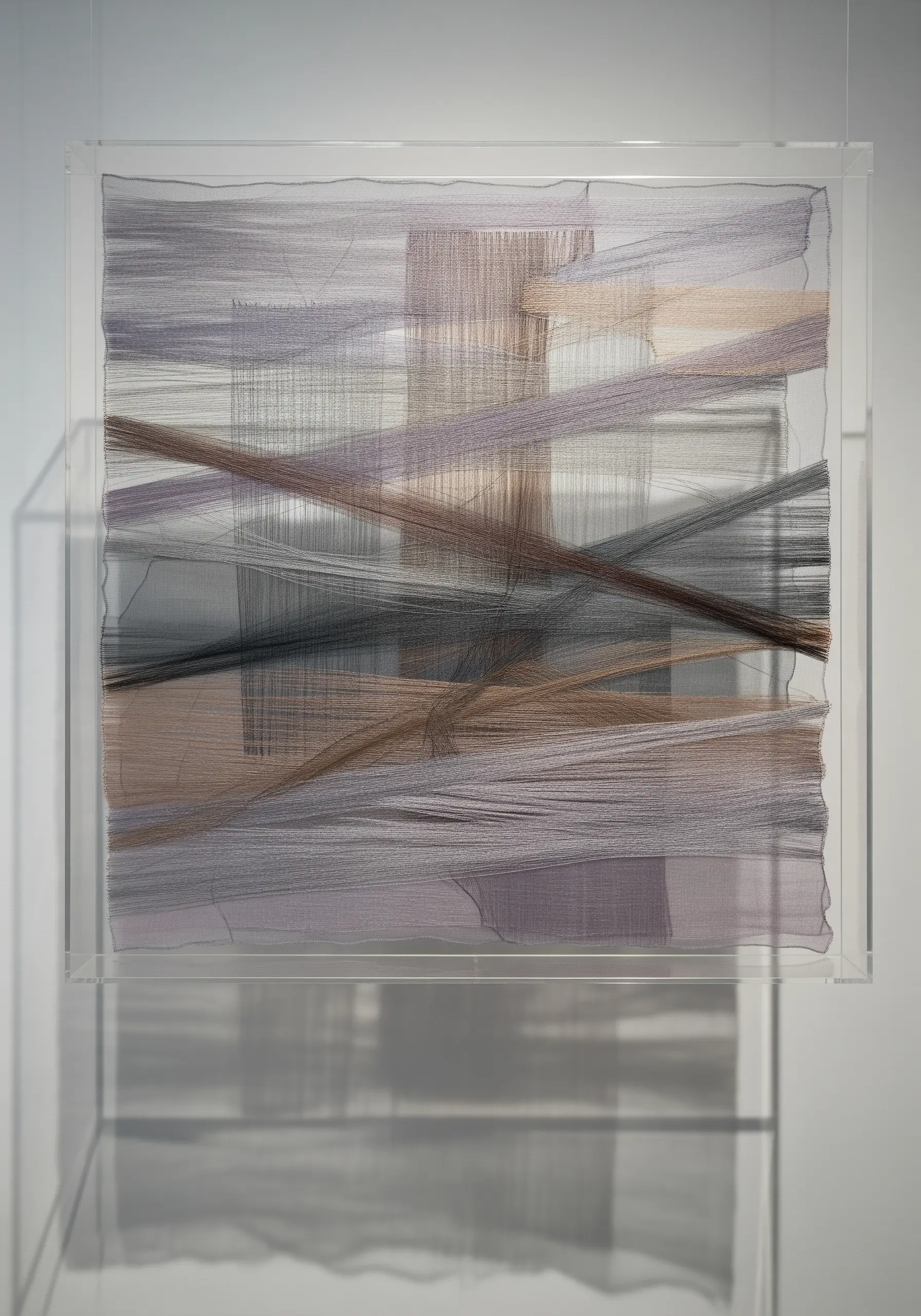 Layered, intersecting threads in neutral tones suspended within a clear acrylic box.