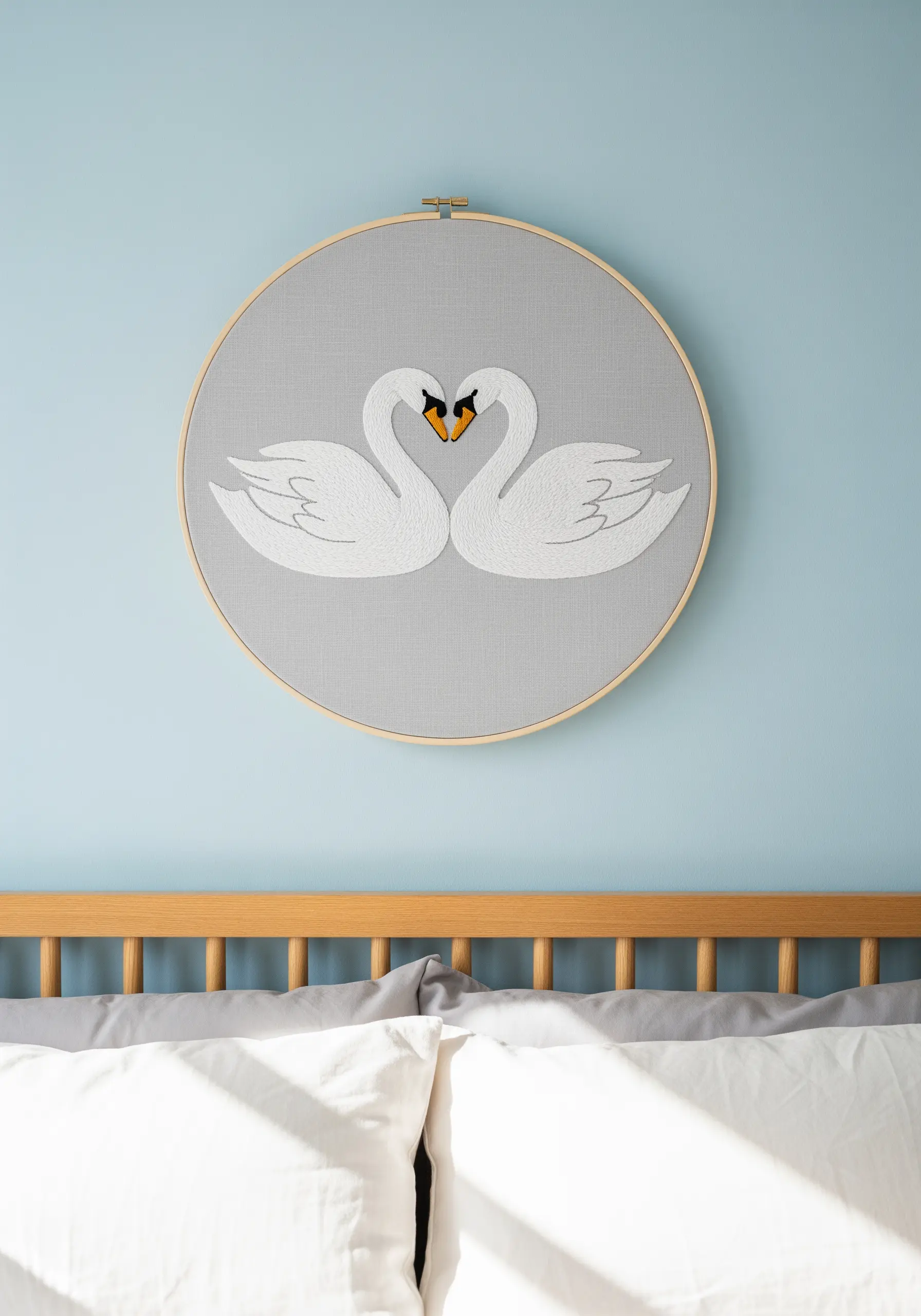 Two white swans facing each other to form a heart shape, embroidered on grey fabric.