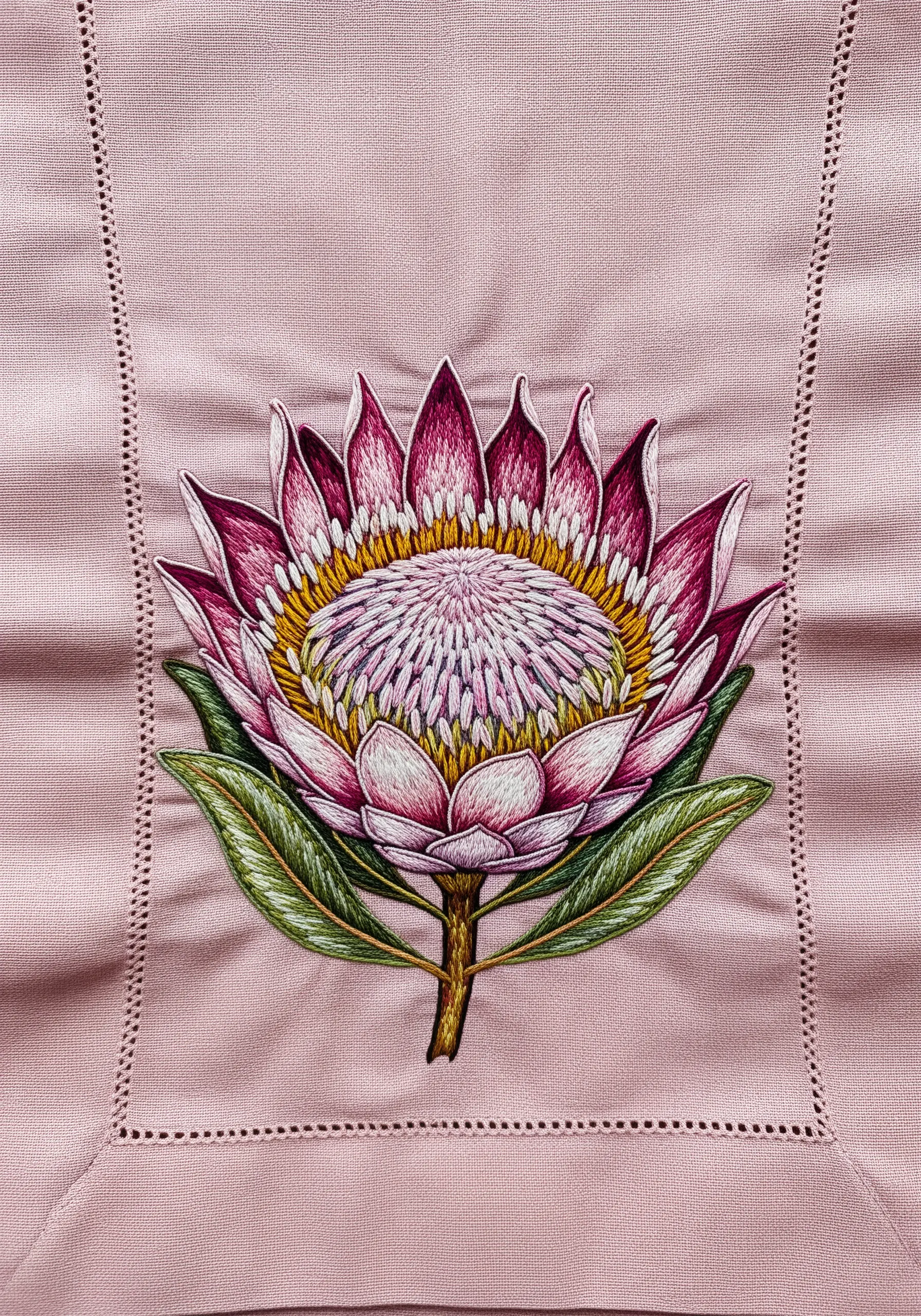 A highly detailed, thread-painted protea flower on a dusty pink tablecloth.