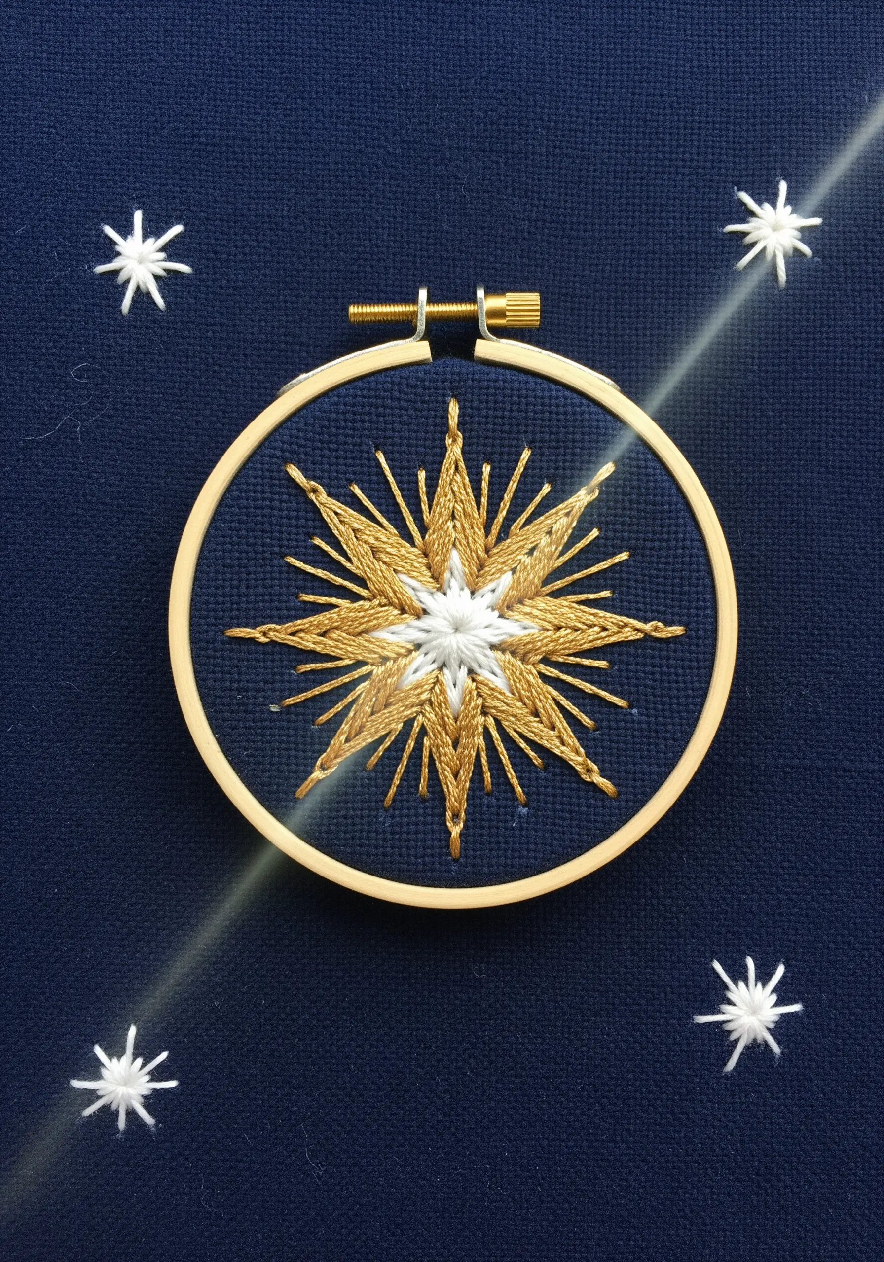 A starburst embroidered with gold and white metallic threads on a navy blue background.