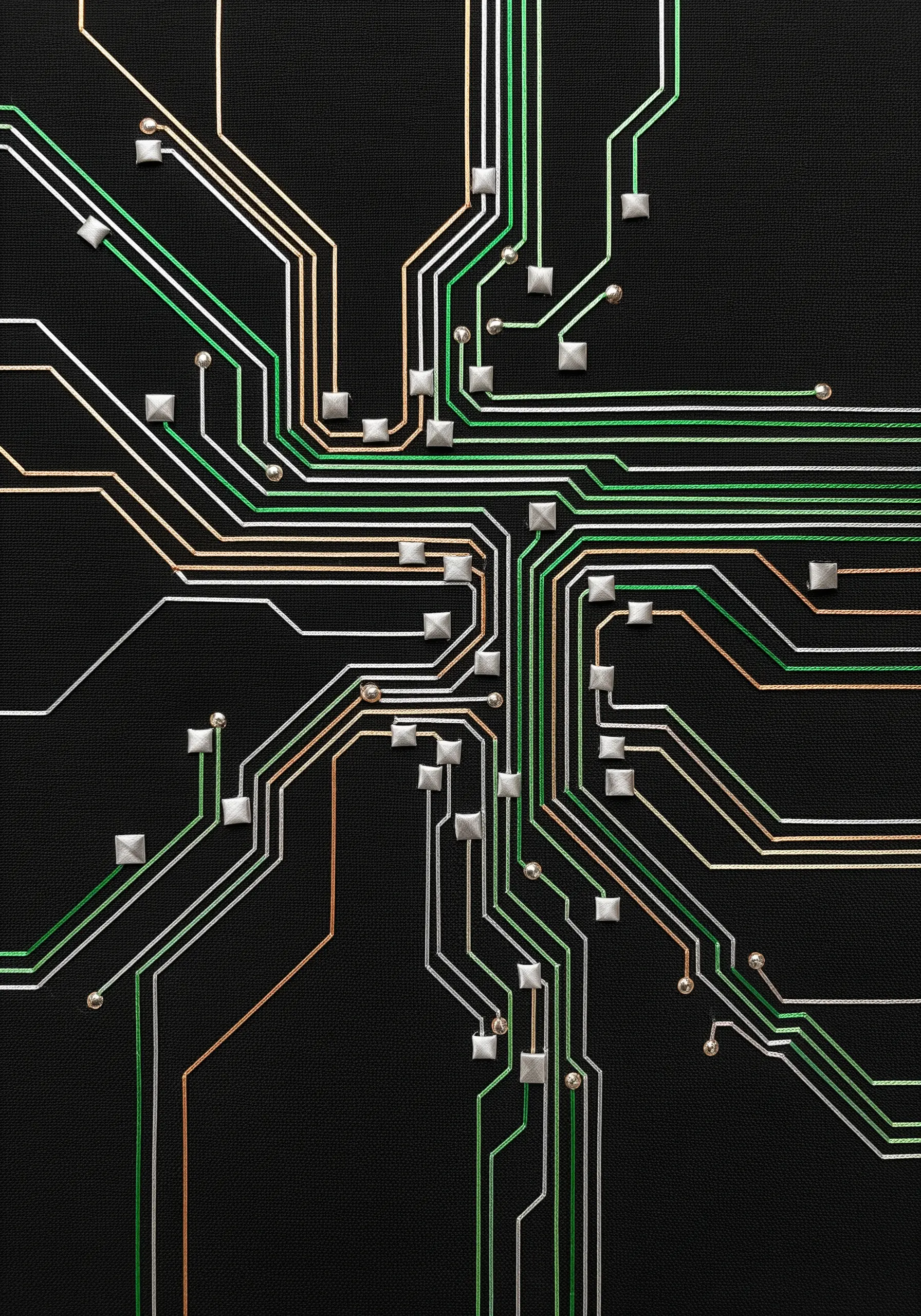An embroidered circuit board pattern with metallic thread lines and square silver beads.