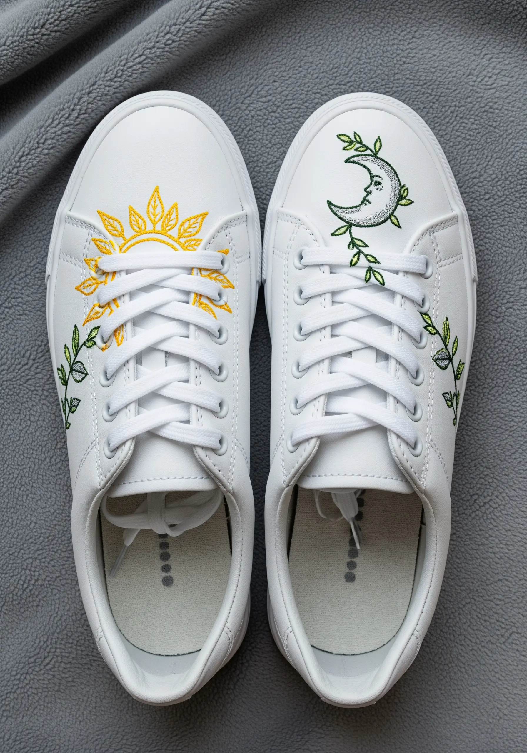 A sun embroidered on one sneaker and a moon on the other, both framed by green vines.