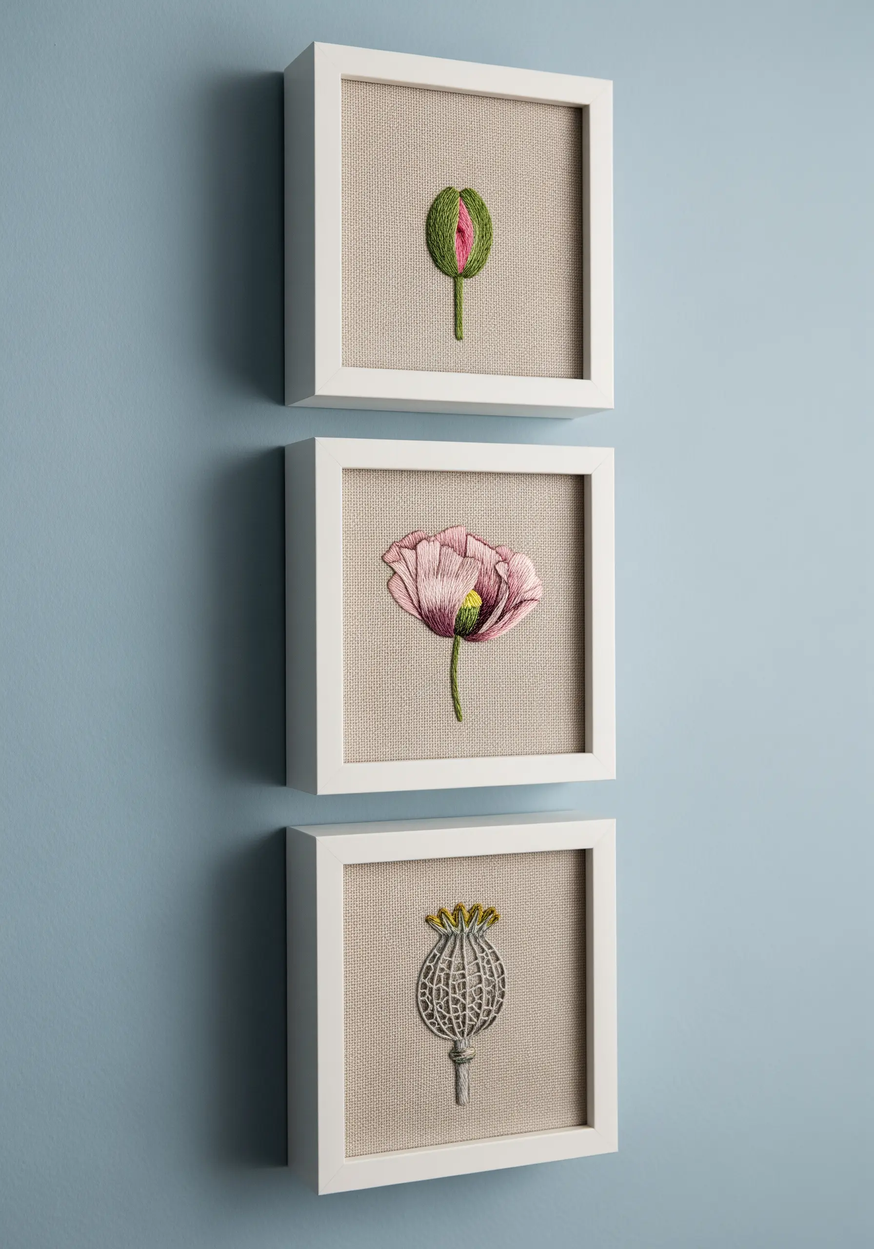 Three small framed embroidery pieces showing a poppy bud, flower, and seed pod.