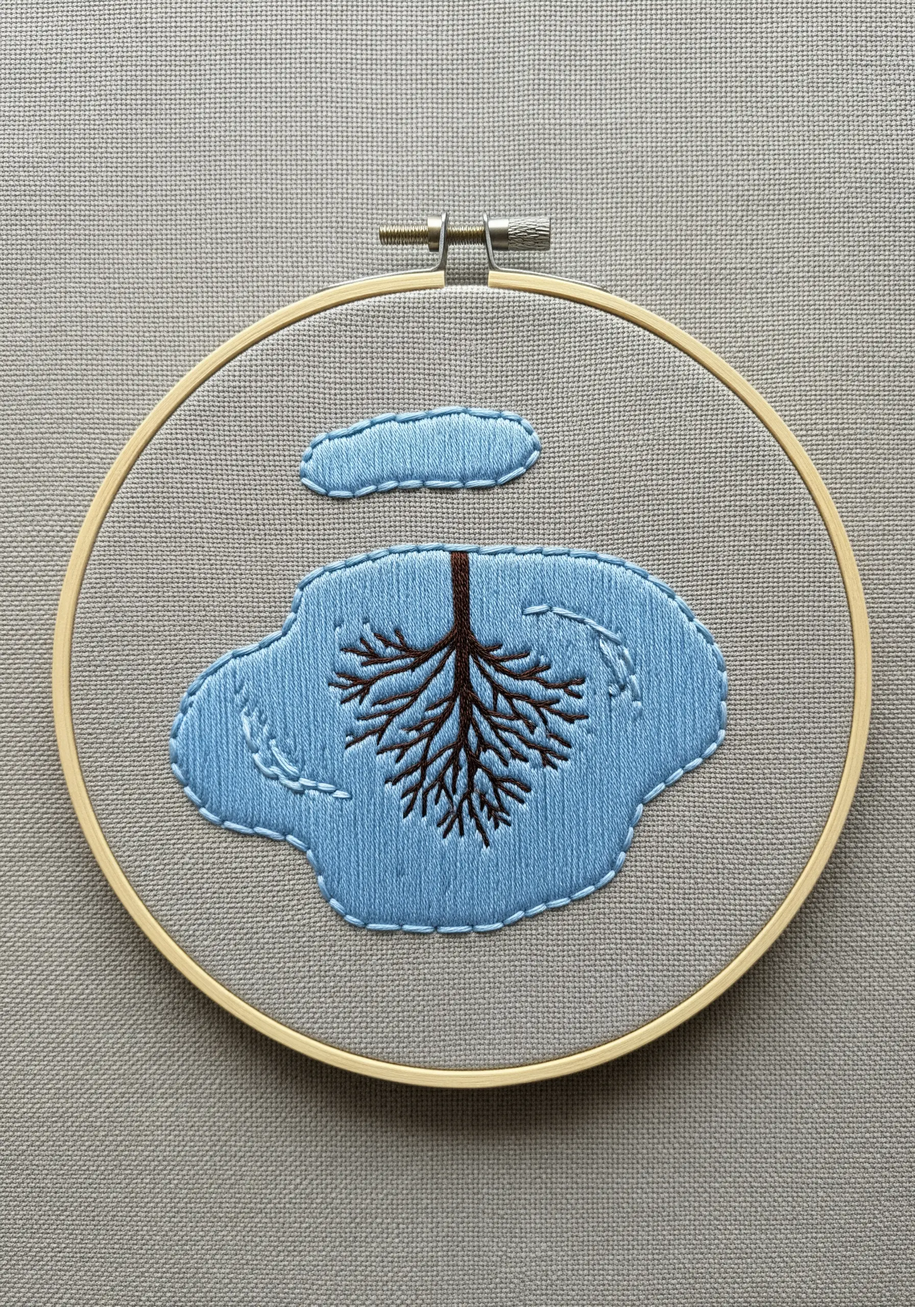 Embroidered puddle reflecting tree roots, with a cloud floating above on gray fabric.