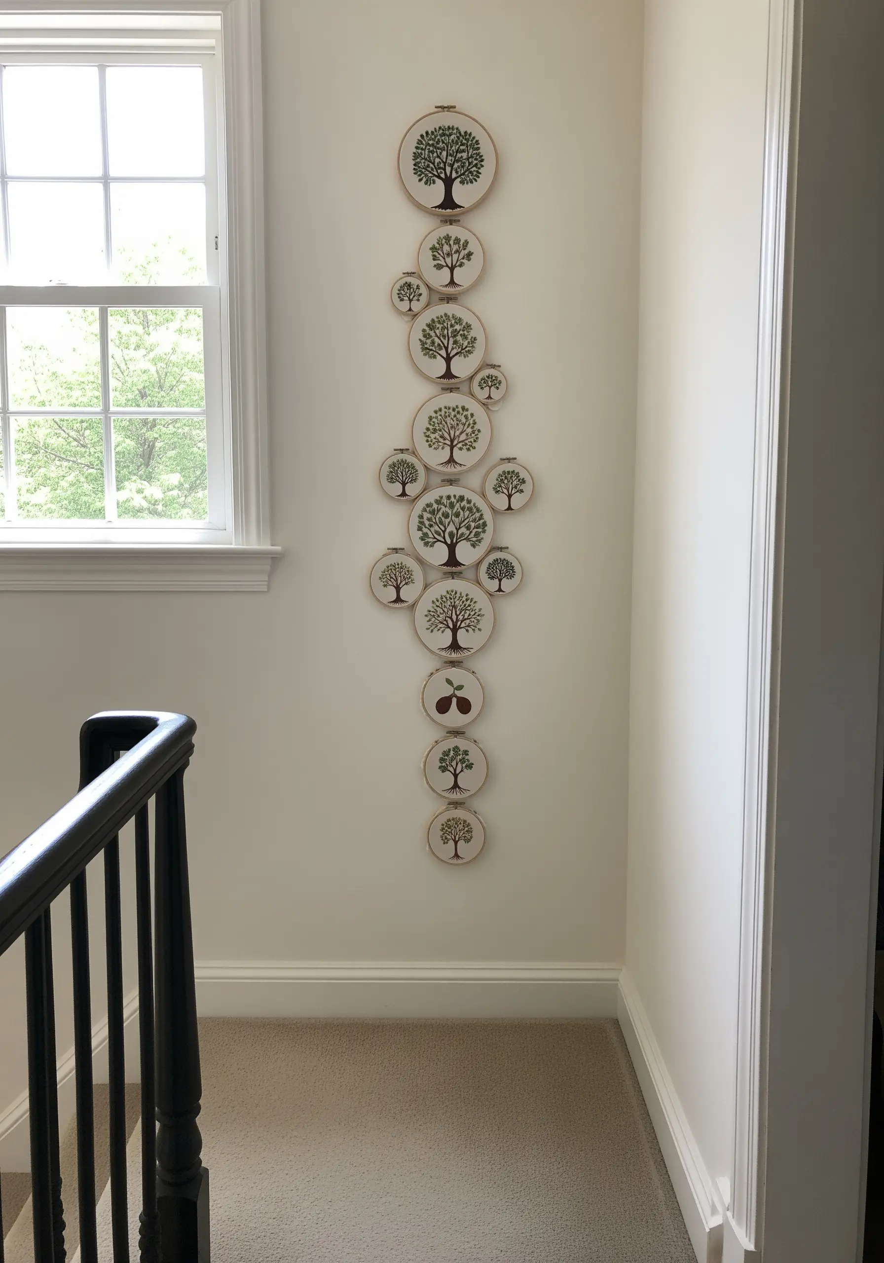 A vertical cascade of embroidery hoops depicting trees of various sizes in a narrow hallway.