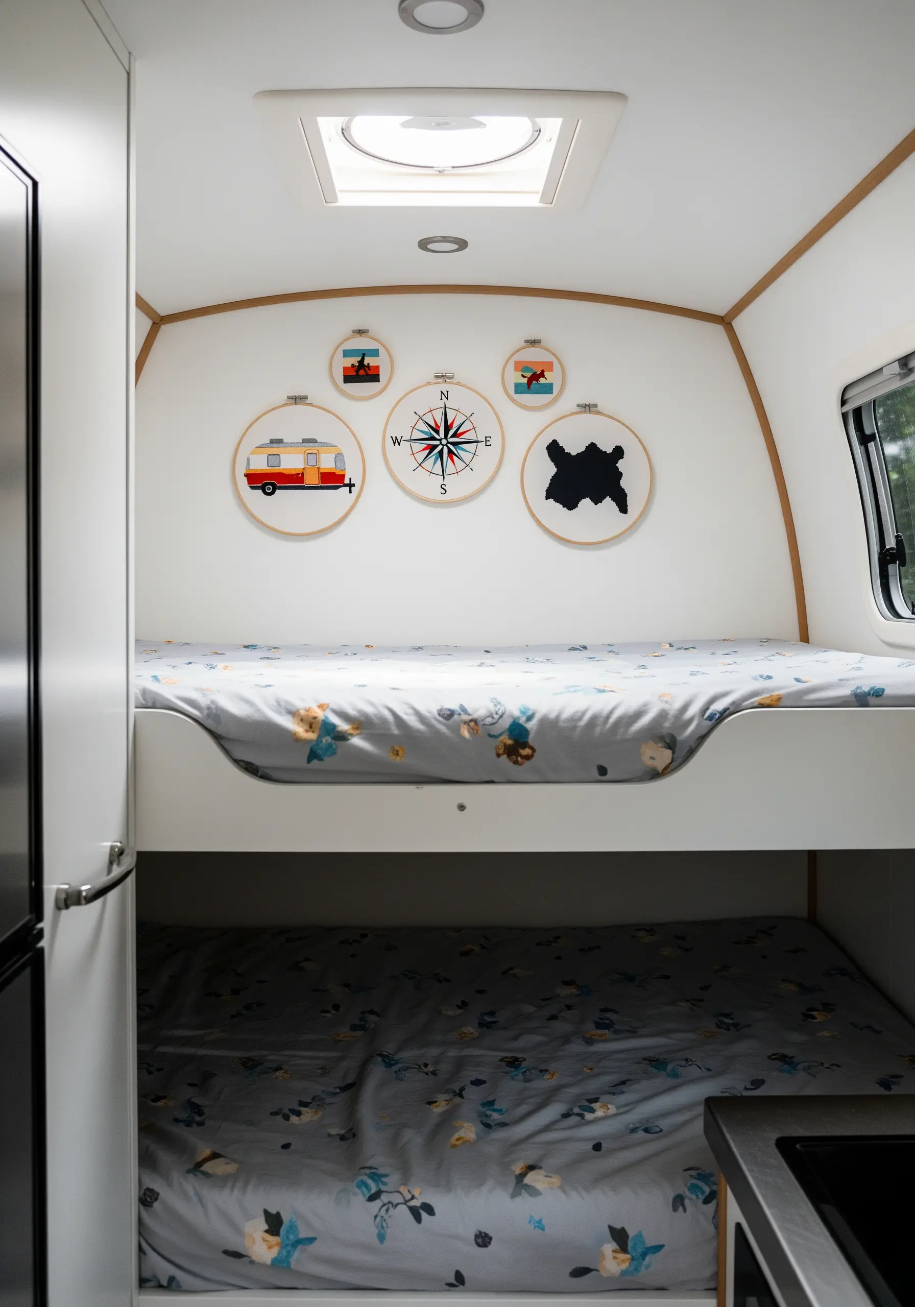 A collection of travel-themed embroidery hoops, including a camper and a compass, inside a caravan