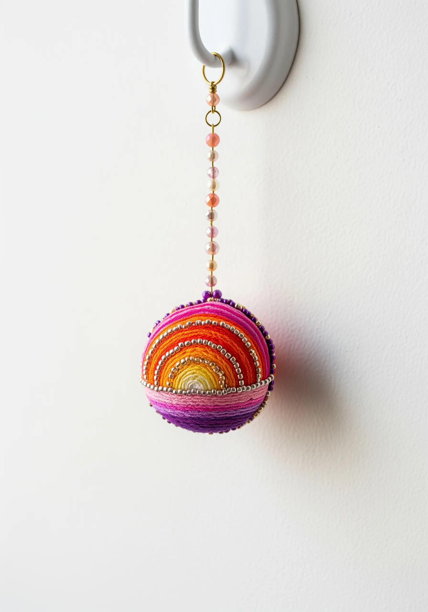 A colorful Temari ball ornament with wrapped thread in sunset hues and silver beads.