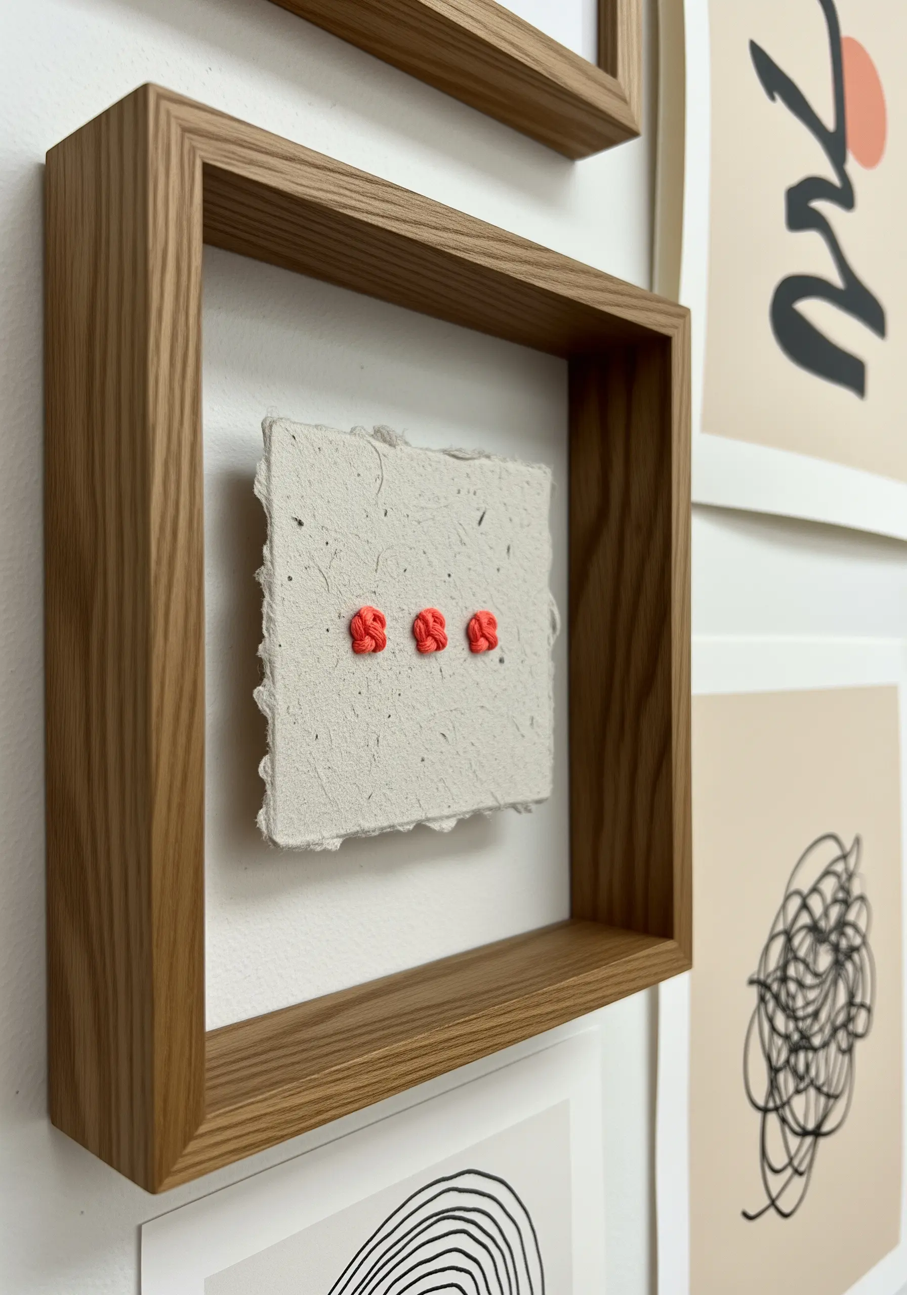 Three bright red French knots embroidered on a small piece of textured handmade paper in a shadowbox.