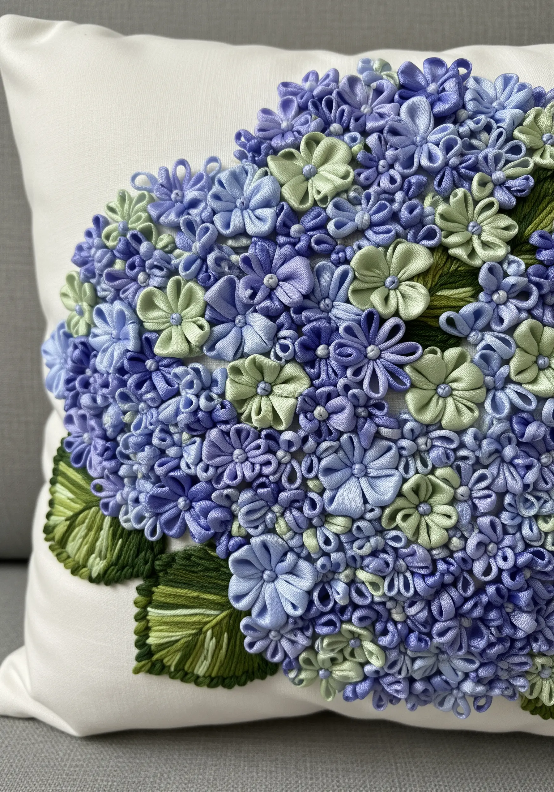 A dense cluster of purple, blue, and green ribbon embroidery hydrangeas on a white pillow.