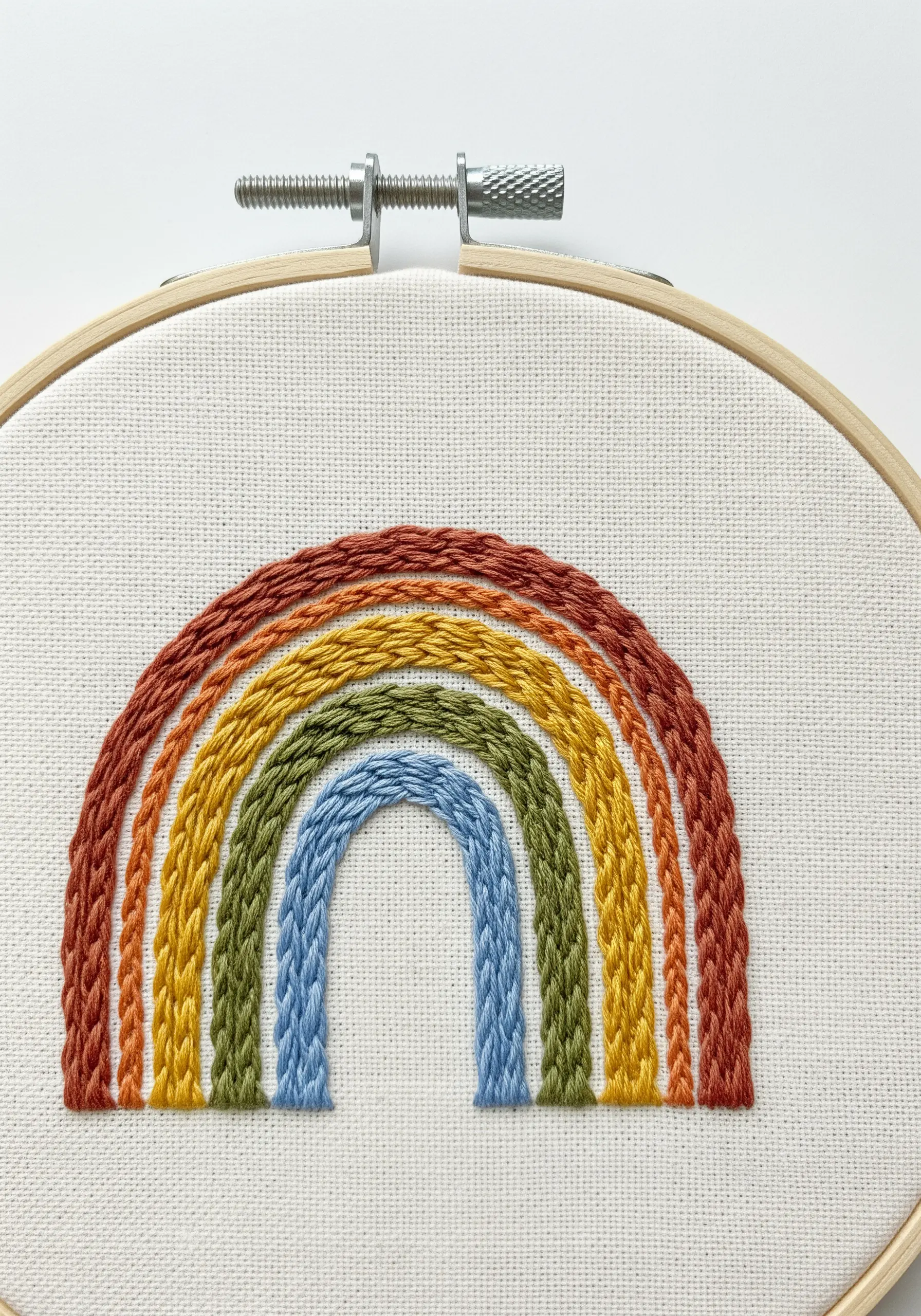 A rainbow embroidered with thick, textured stitches in earthy tones.