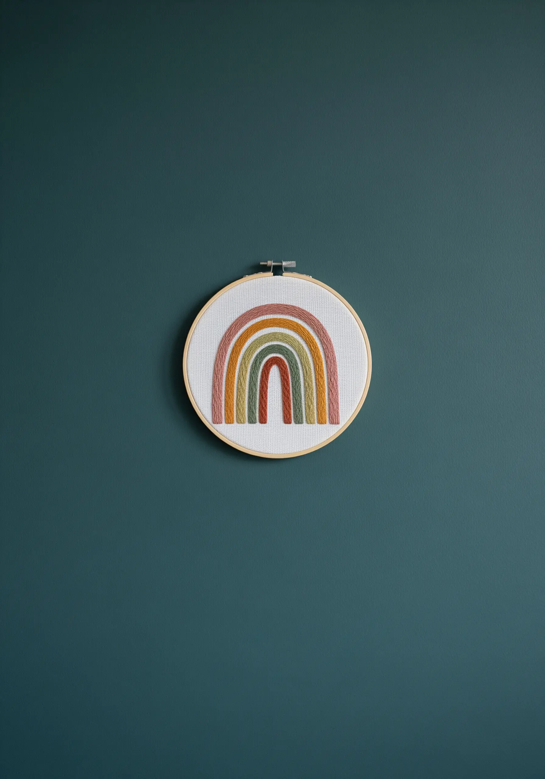 A small, textured rainbow with earthy tones embroidered on a white background.