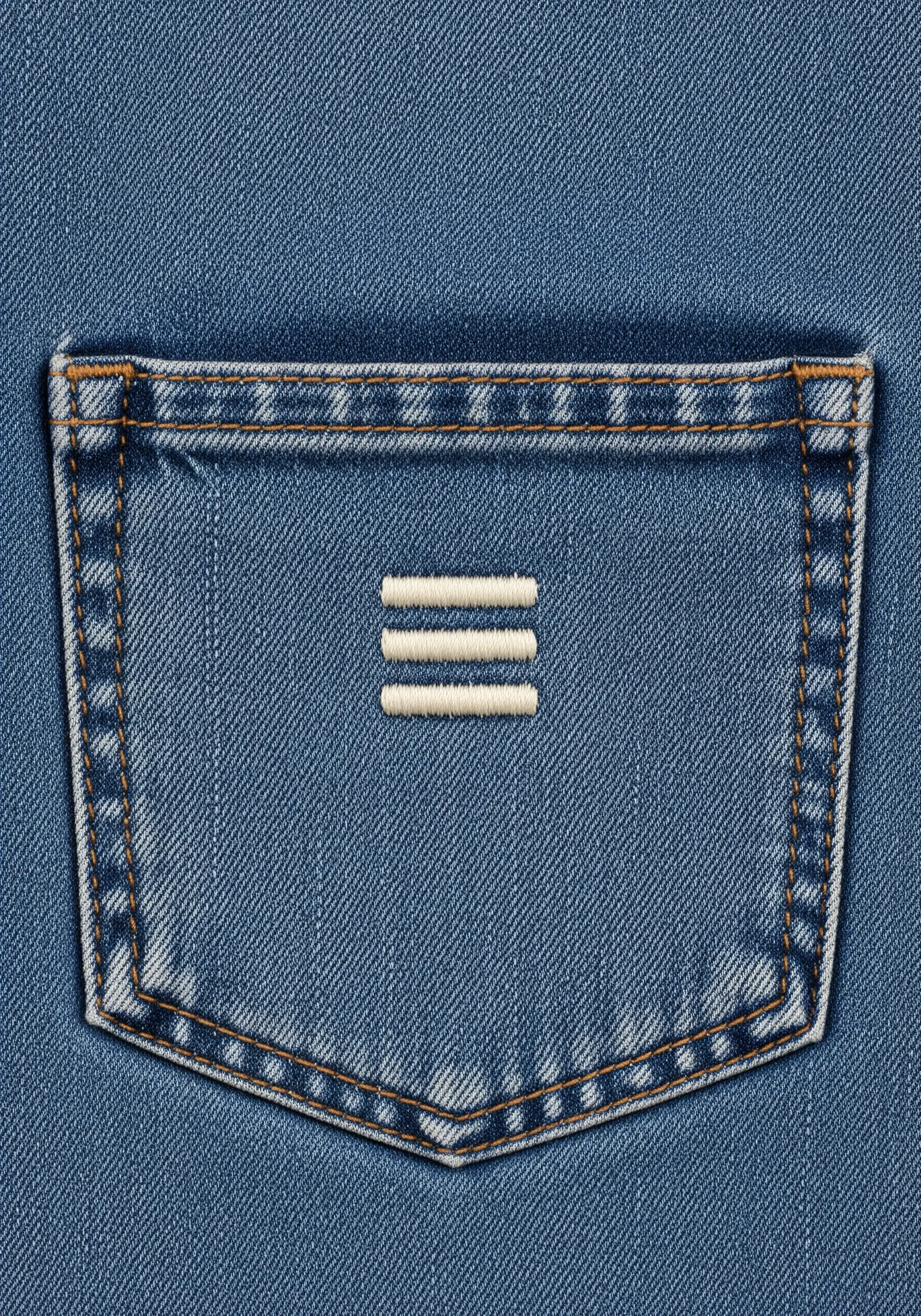 Three short, horizontal white bars stitched in the center of a denim pocket.