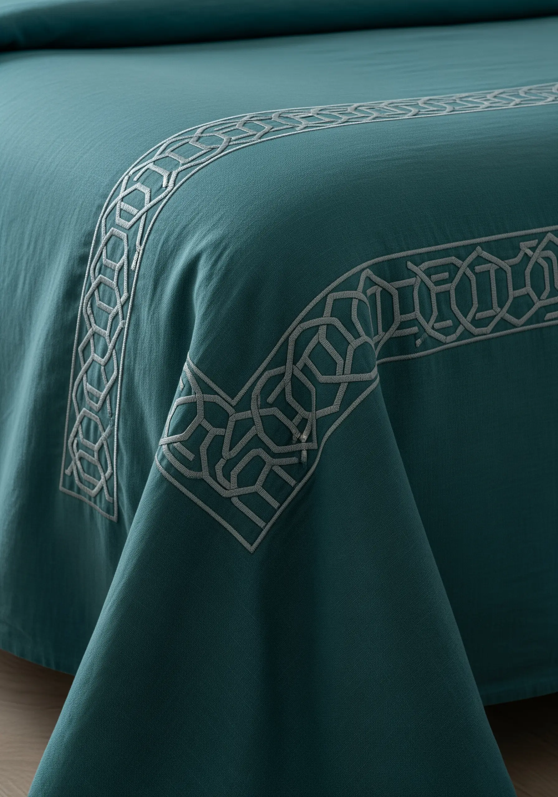 A silver-grey geometric Art Deco border embroidered on the edge of a teal bedsheet.