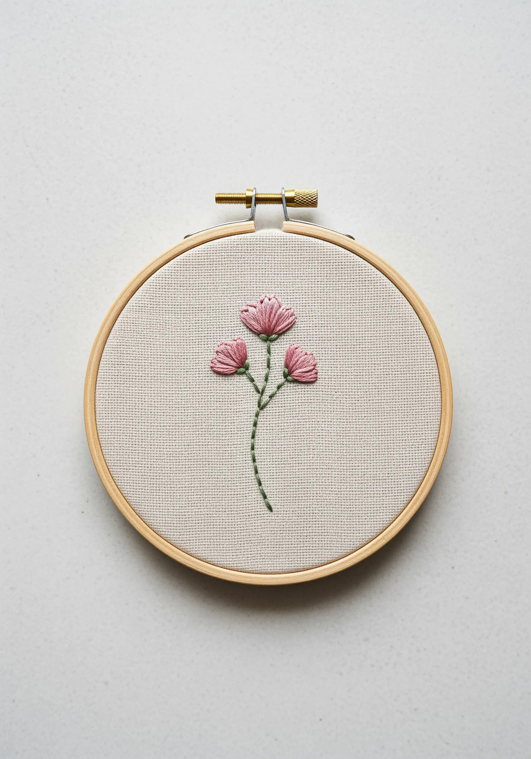 Three minimal pink flowers embroidered on neutral linen with directional satin stitch.