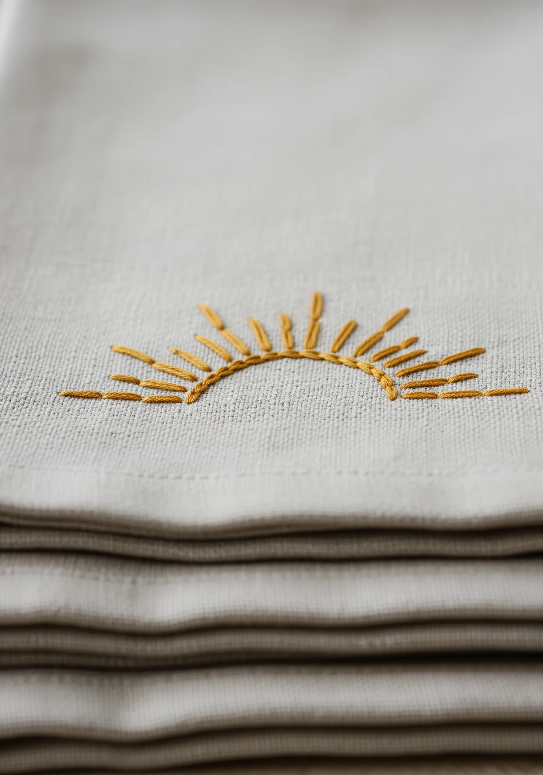 A minimalist embroidered sun with straight stitch rays on a neutral linen fabric.
