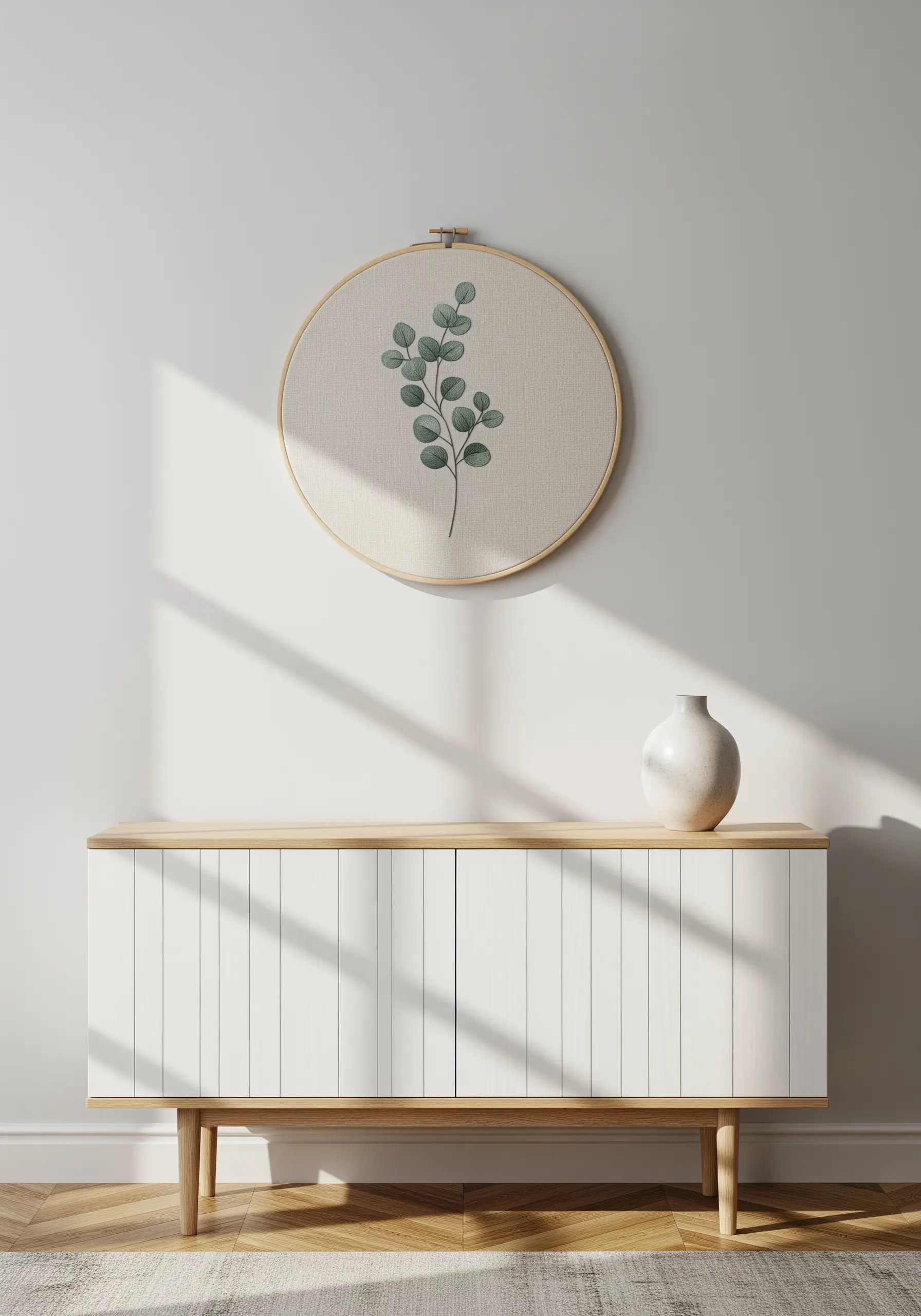 Minimalist eucalyptus branch embroidered on natural linen in a wooden hoop.