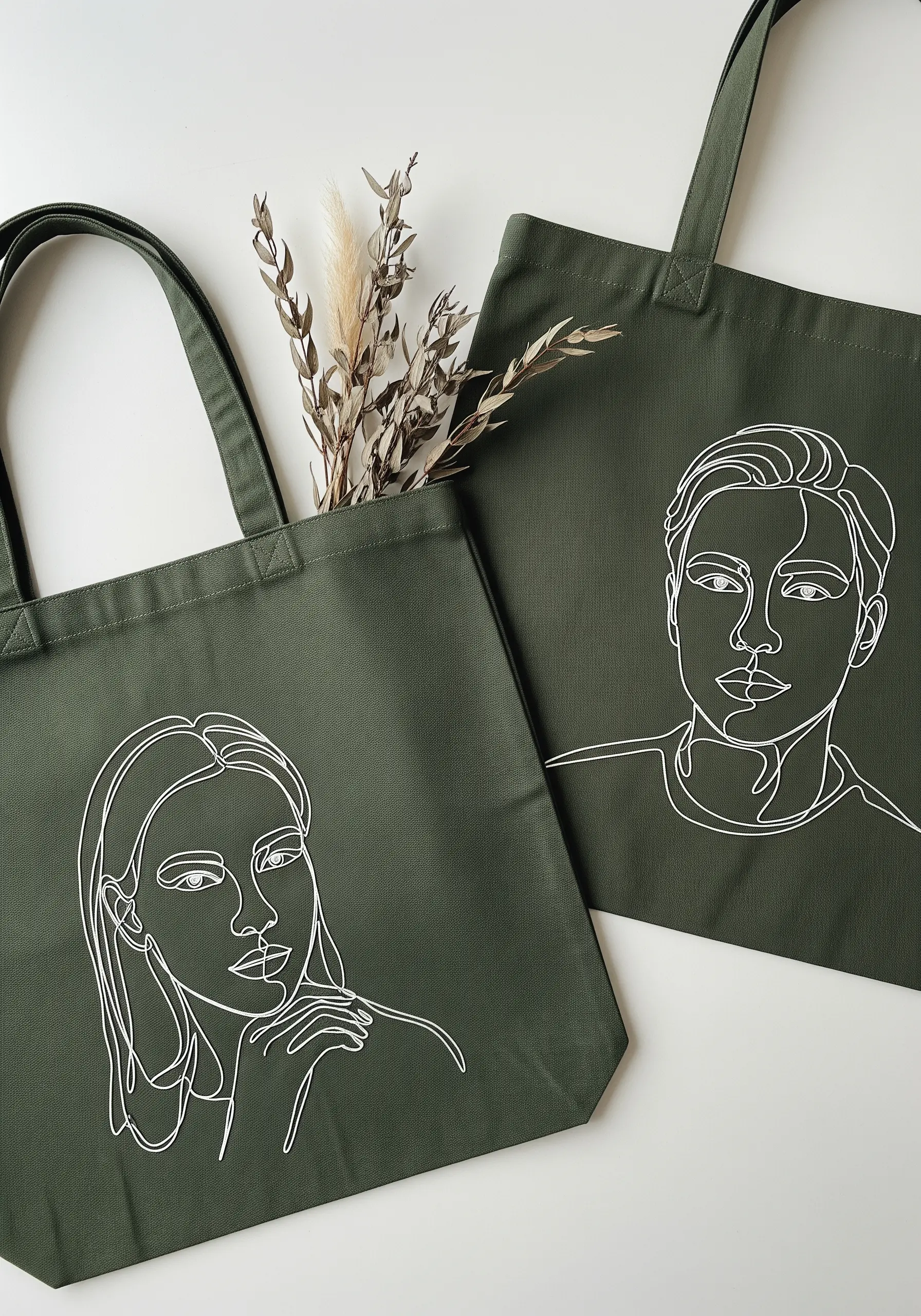 Olive green tote bags featuring minimalist single-line embroidered portraits.