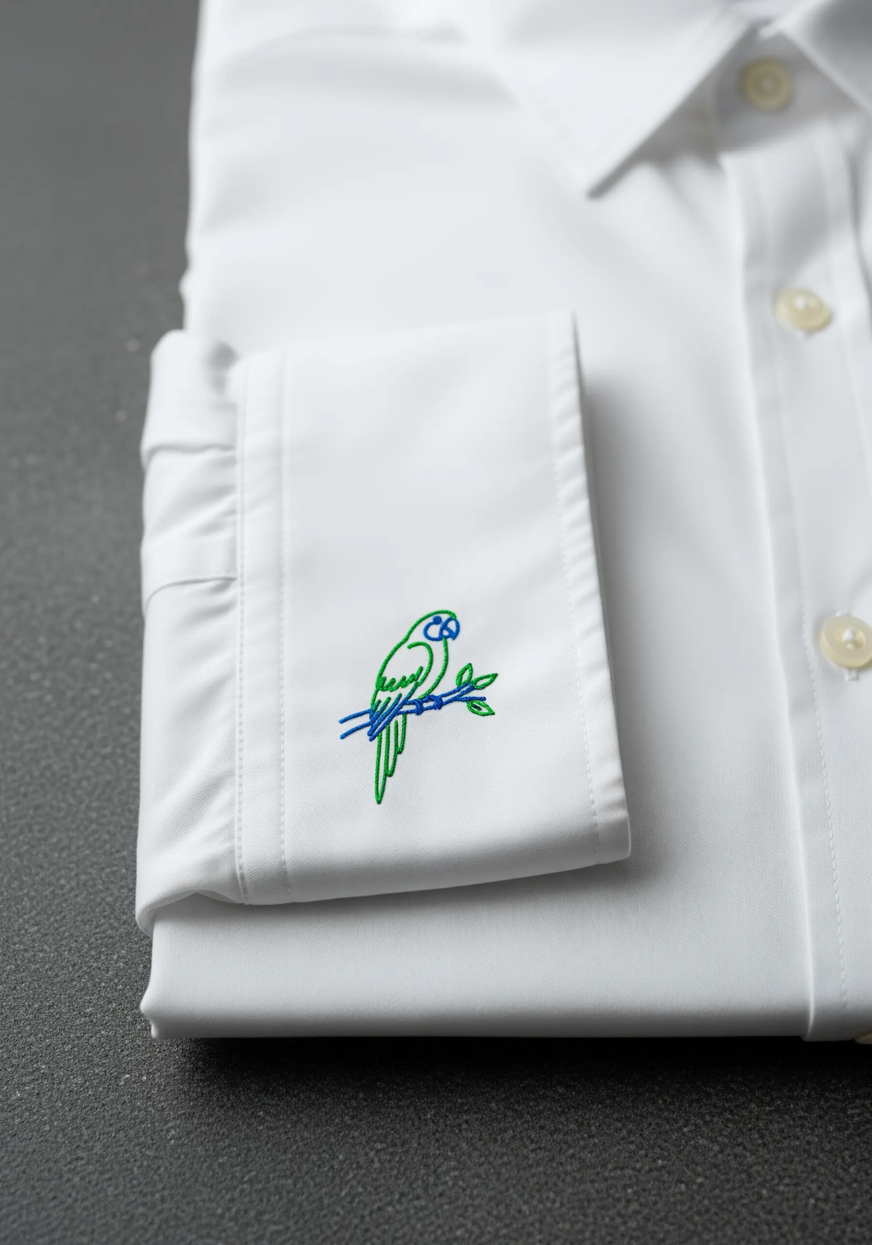 A small, two-color line art parrot embroidered on a white shirt cuff.
