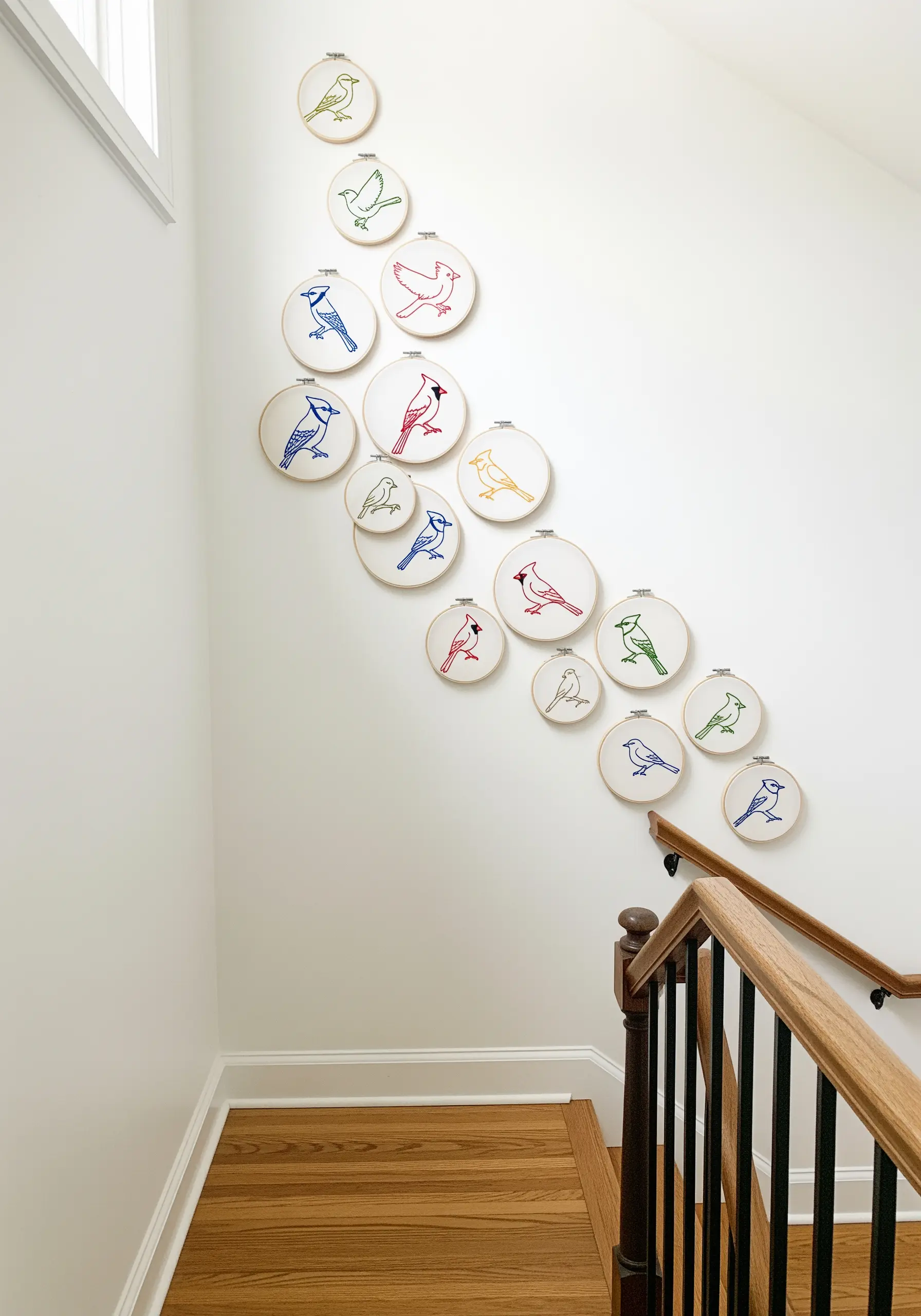 A collection of embroidery hoops with simple, colorful bird outlines ascending a staircase wall.