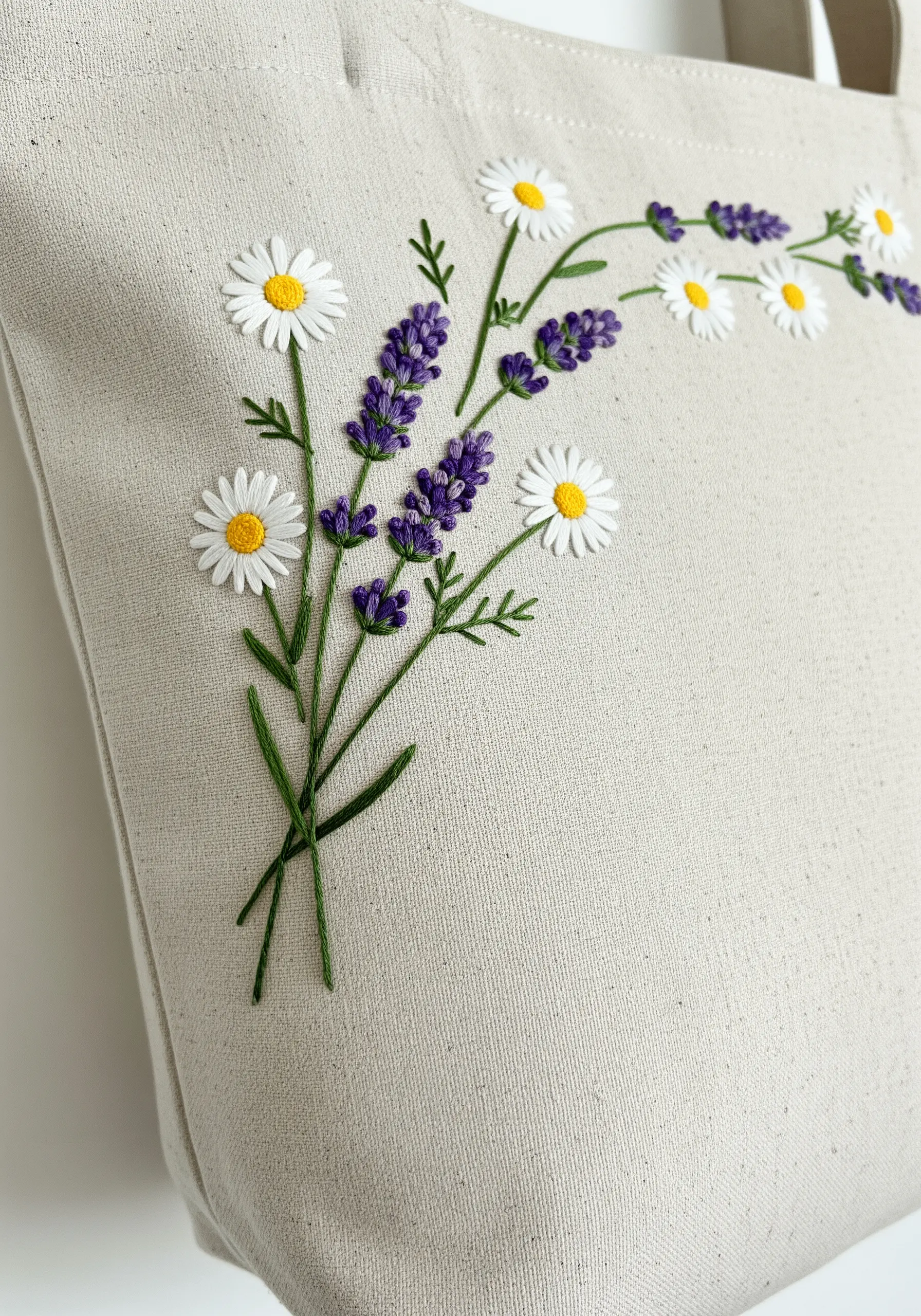 An asymmetrical bouquet of embroidered daisies and lavender in the corner of a tote.