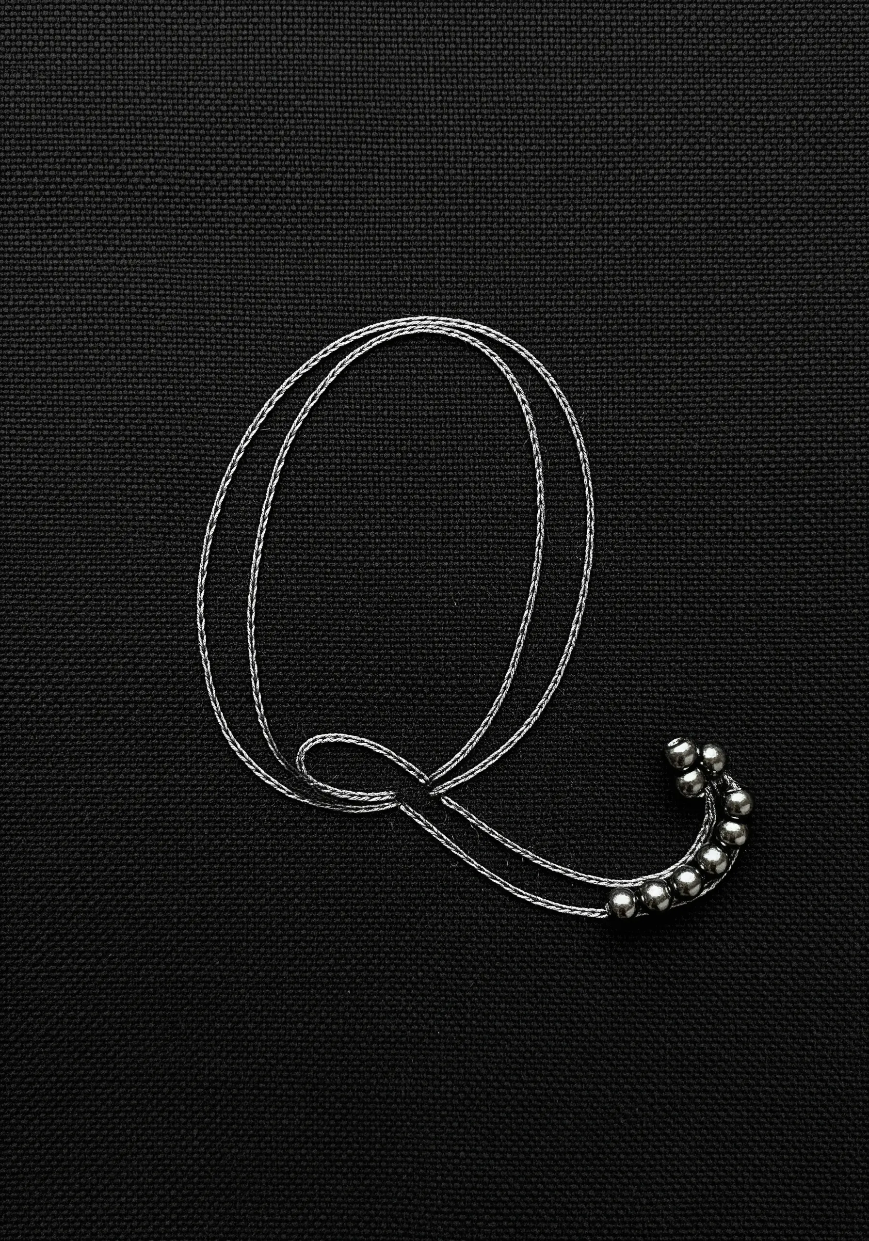 Cursive 'Q' monogram made of silver thread and embellished with silver beads.