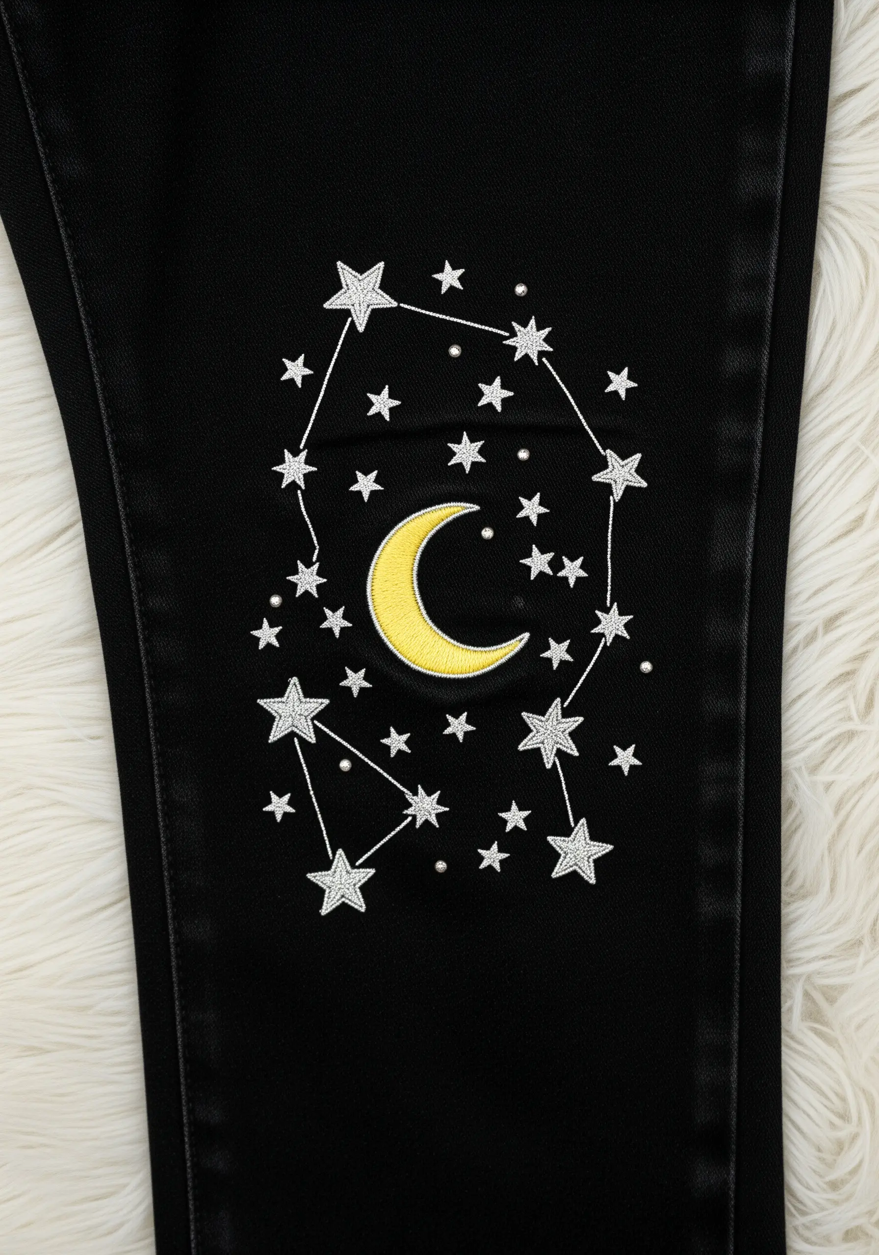 An embroidered constellation with a crescent moon on black denim.