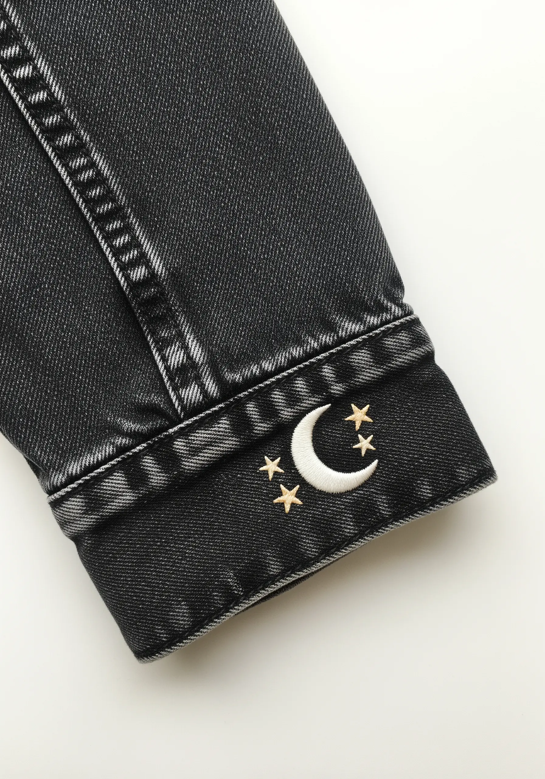 Embroidered crescent moon and tiny gold stars on the cuff of a black denim jacket