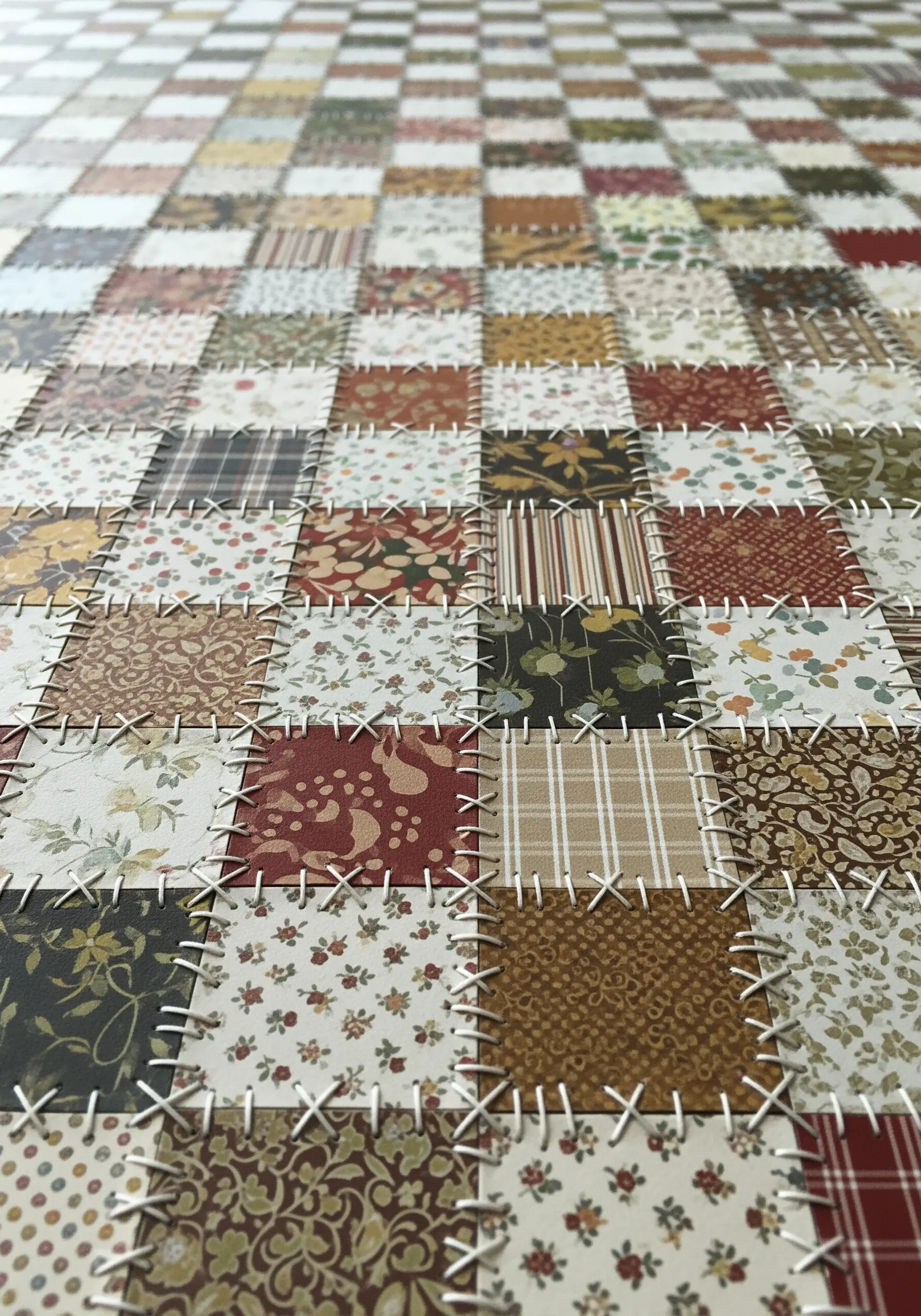 A paper patchwork quilt with each square joined by a visible white cross stitch.