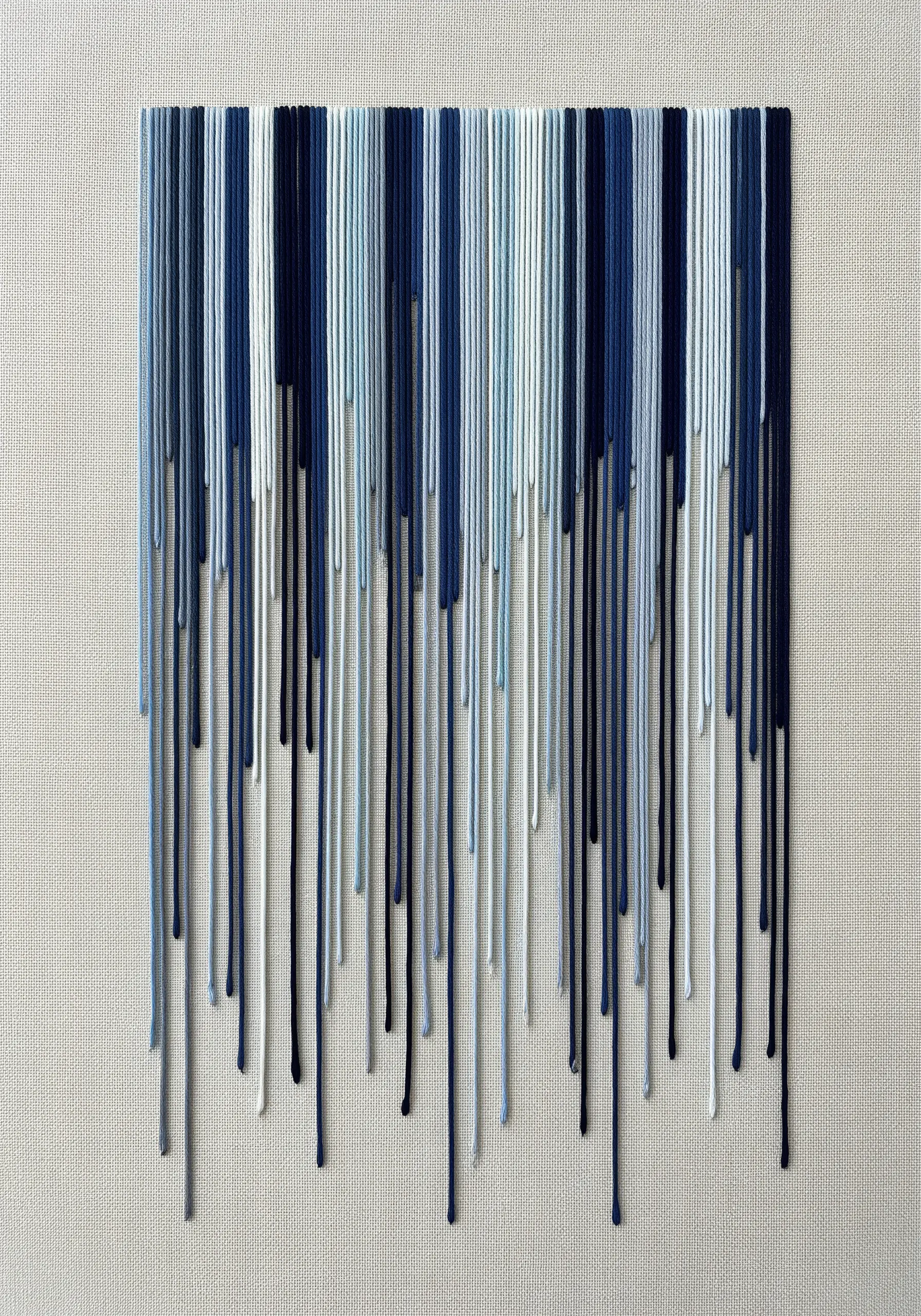 Abstract embroidery with long, cascading blue and white threads creating a fringe effect.