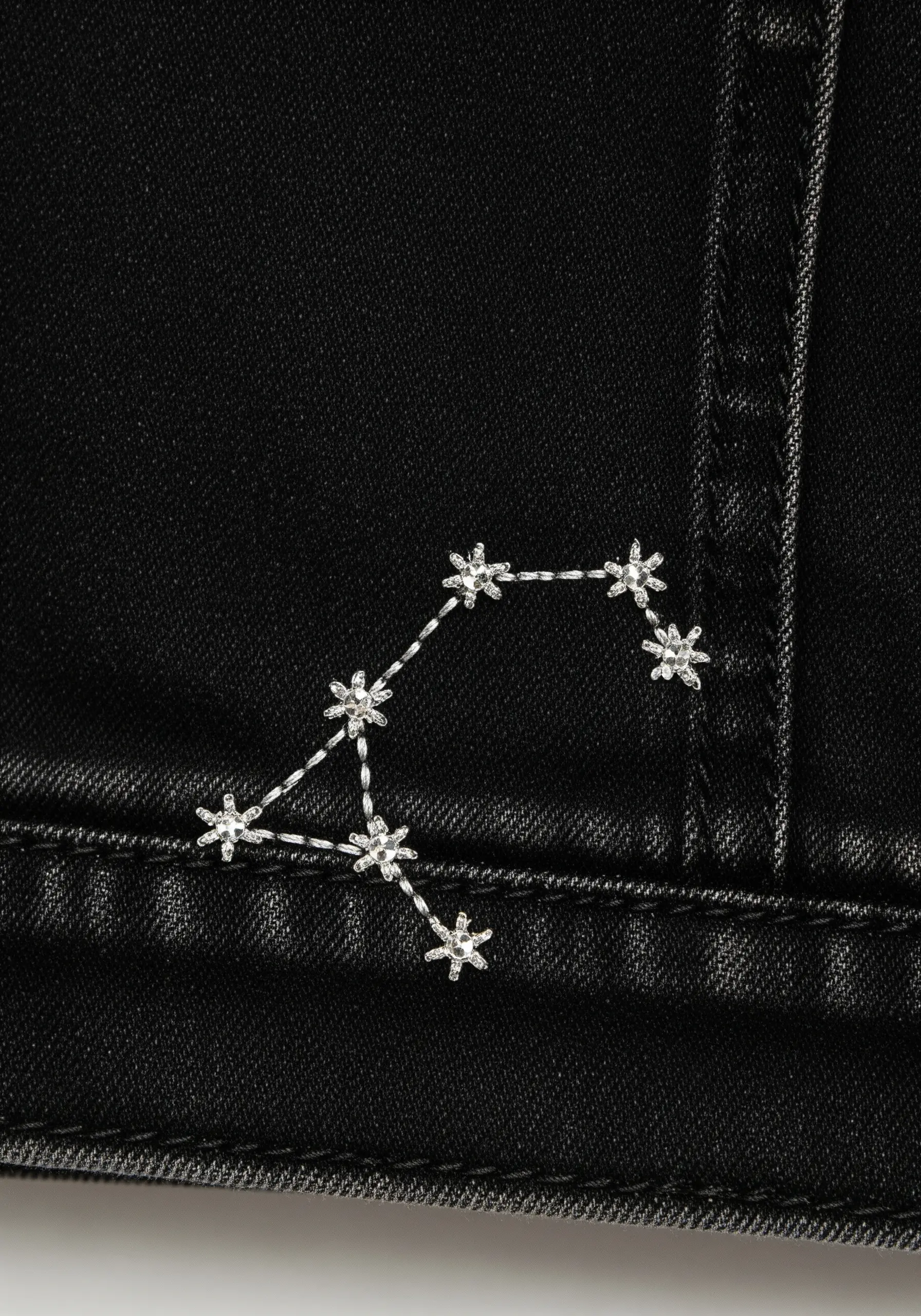 A constellation embroidered in silver thread on the shoulder of a black denim jacket