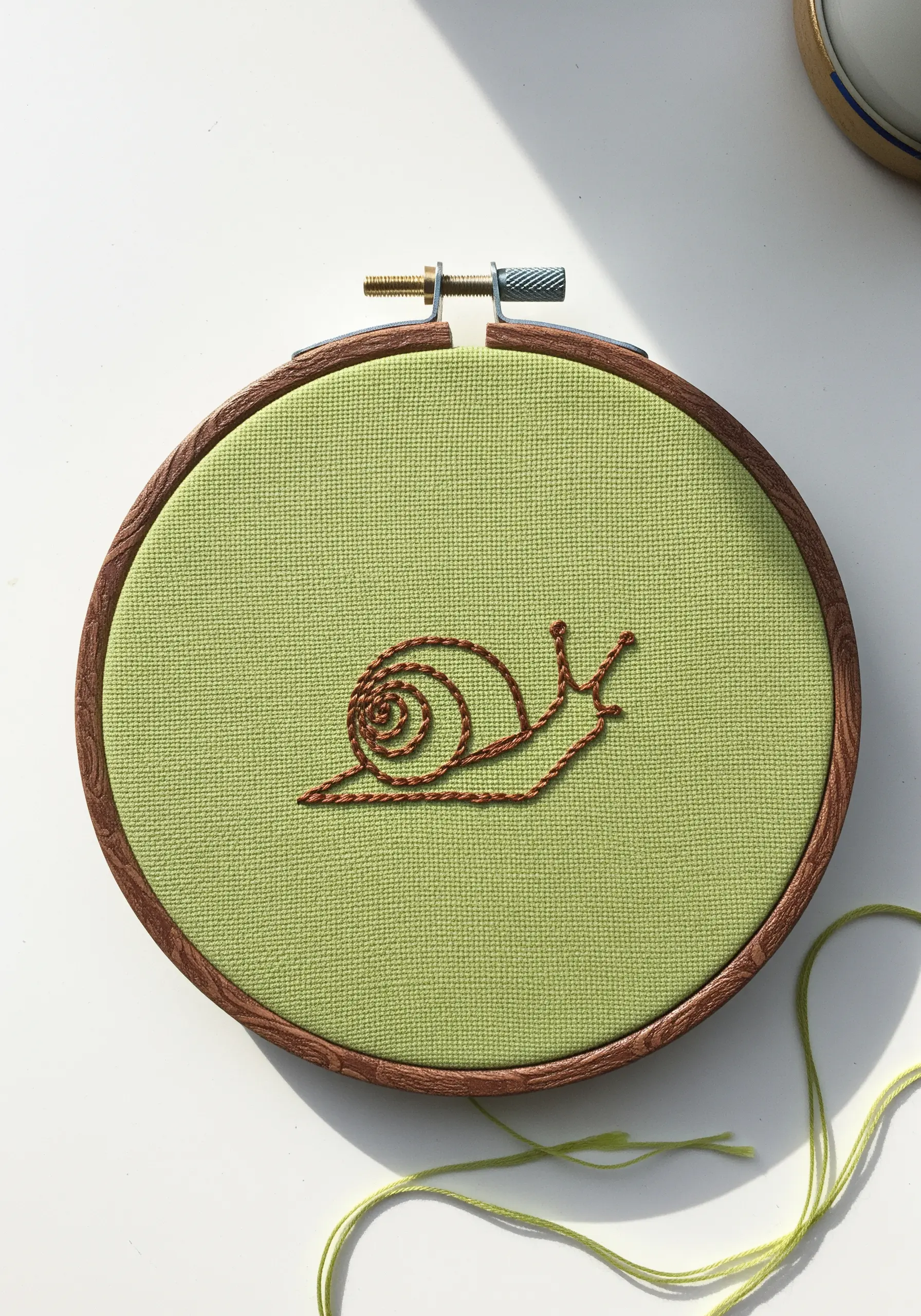 A simple line-art snail embroidered in brown thread on light green fabric.