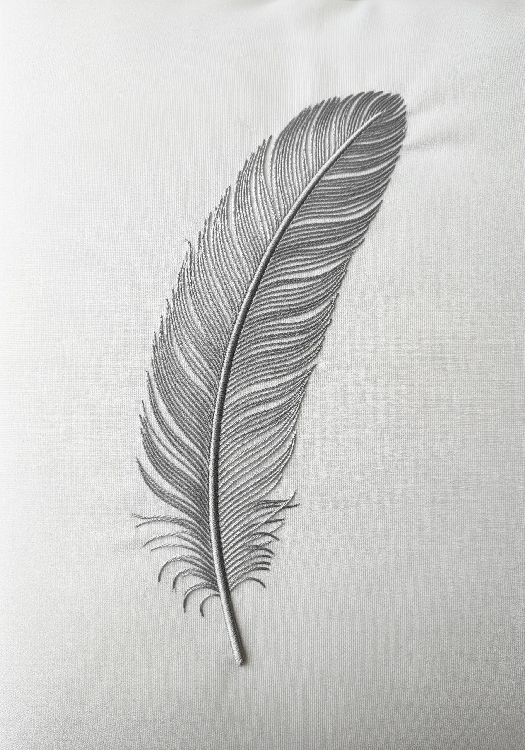 A detailed grey feather embroidered on white fabric, with fine lines creating a soft texture.