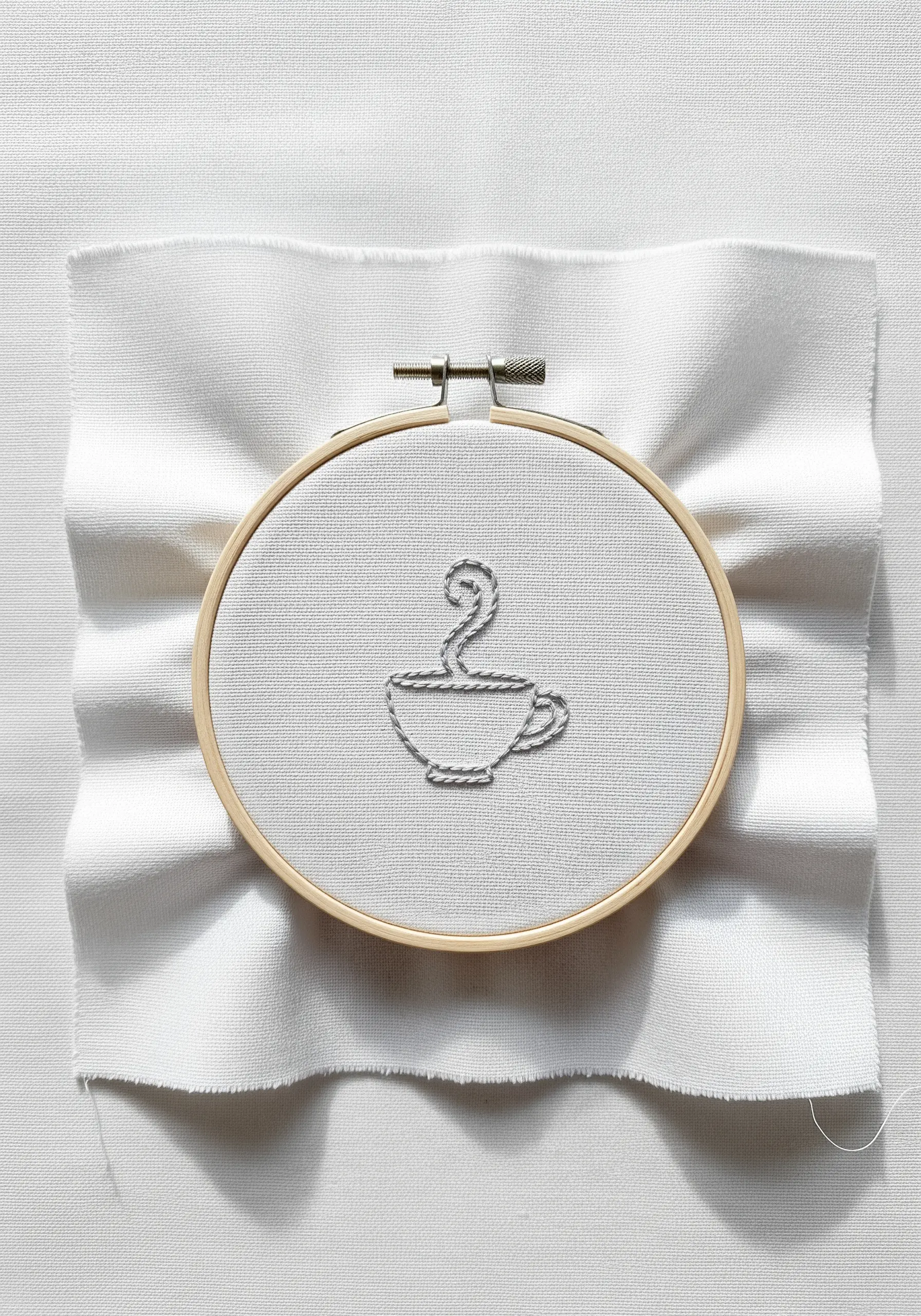 A minimalist steaming coffee cup embroidered in a single, continuous gray line.